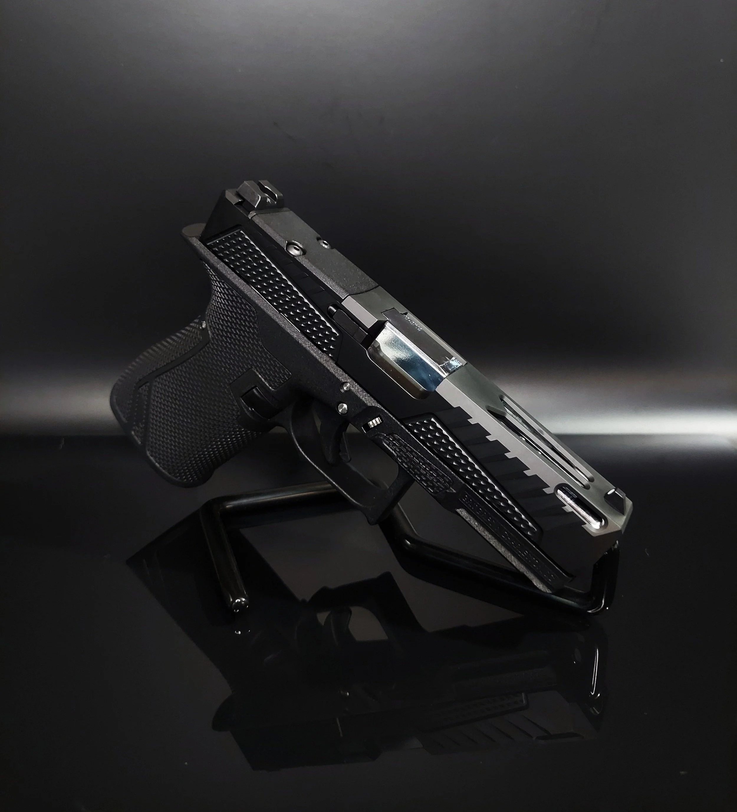 A black semi-automatic pistol placed on a black stand with a reflective surface.
