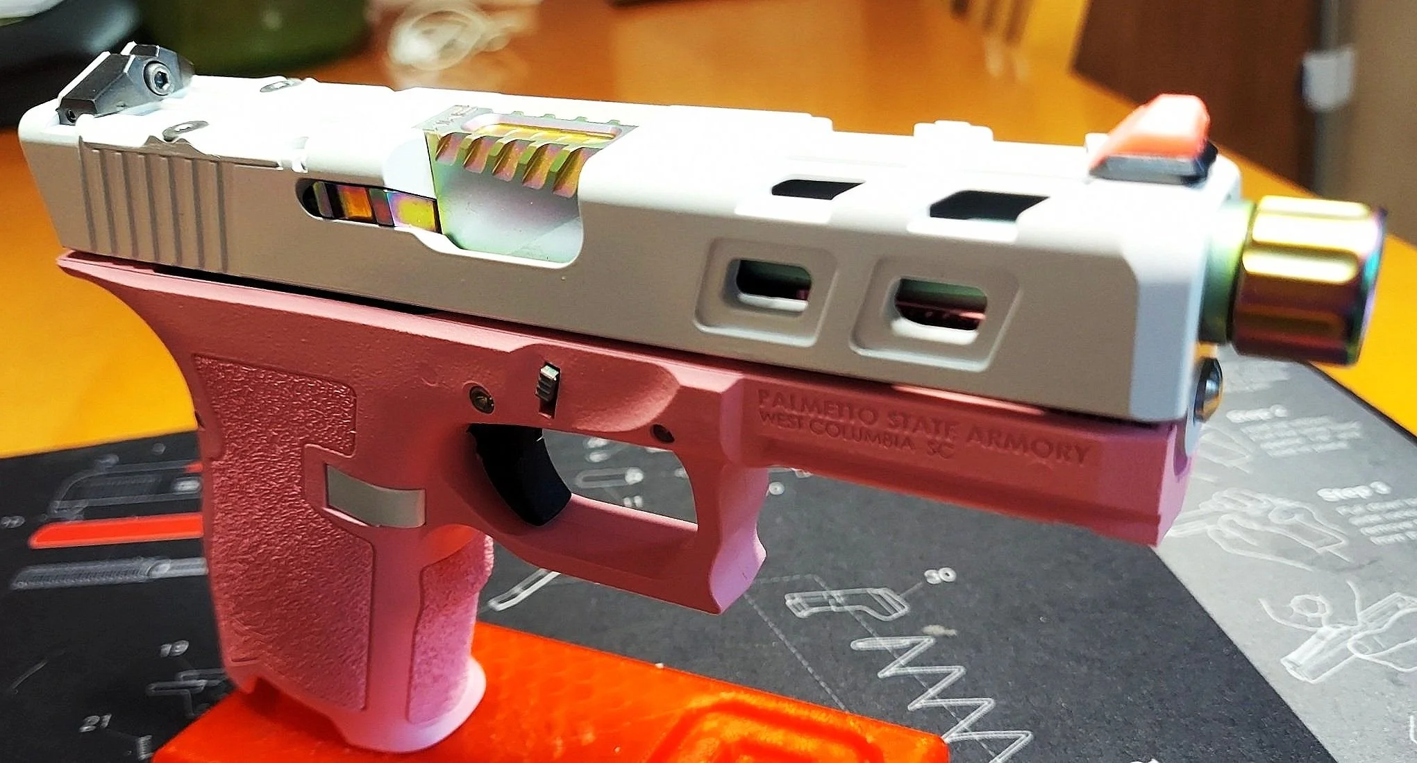 A semi-automatic pistol with a silver slide and pink frame resting on a workbench with tools and guides.