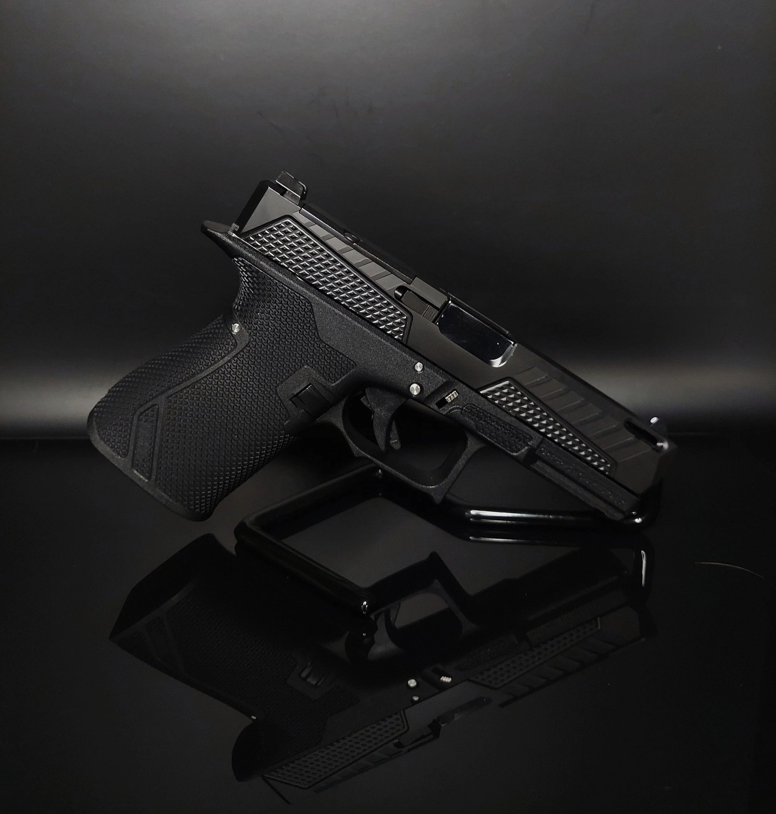 A black semi-automatic pistol resting on a reflective black surface with a dark background.