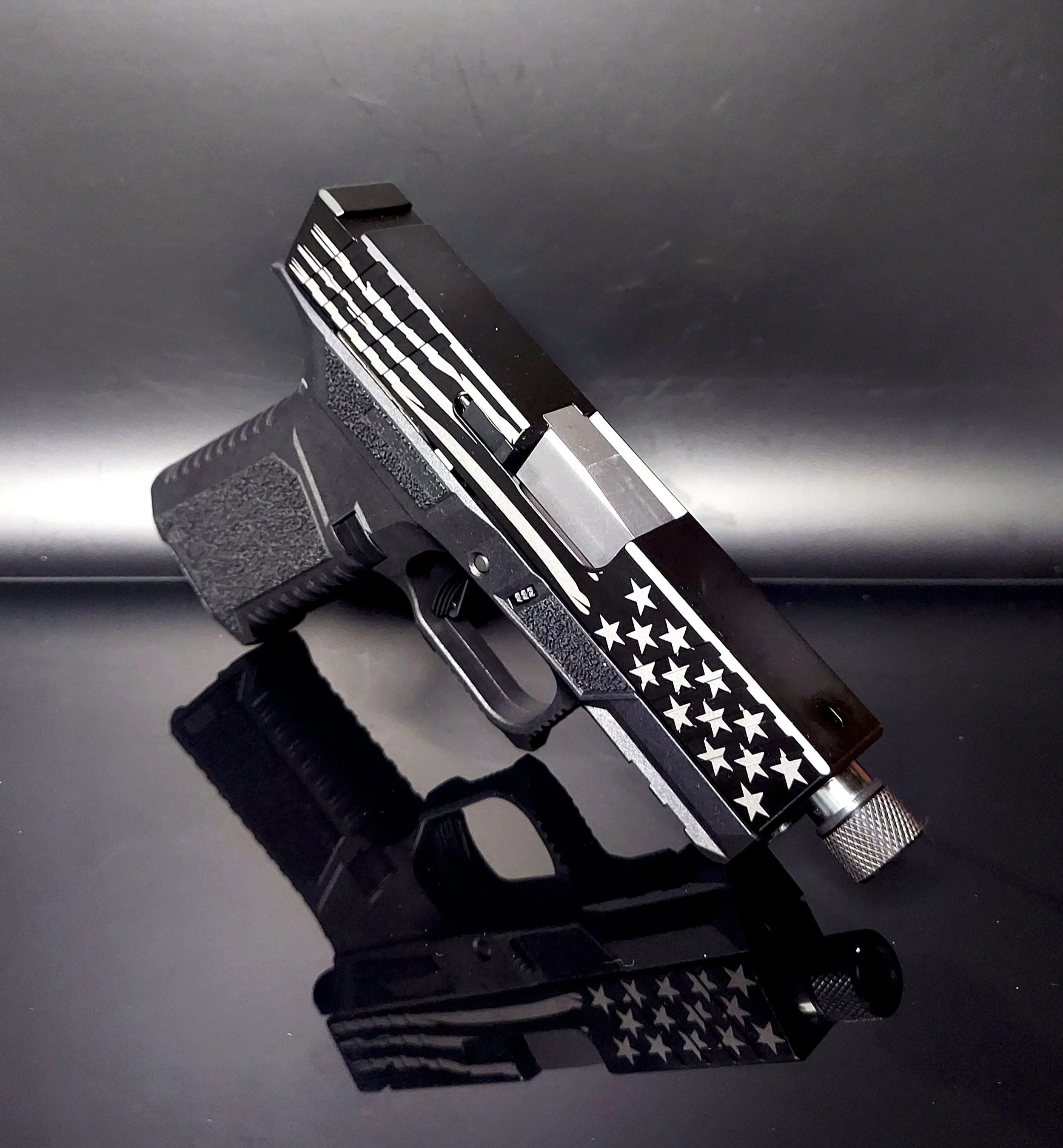 A semi-automatic handgun with a black, white, and silver star-spangled design, resting on a reflective black surface.
