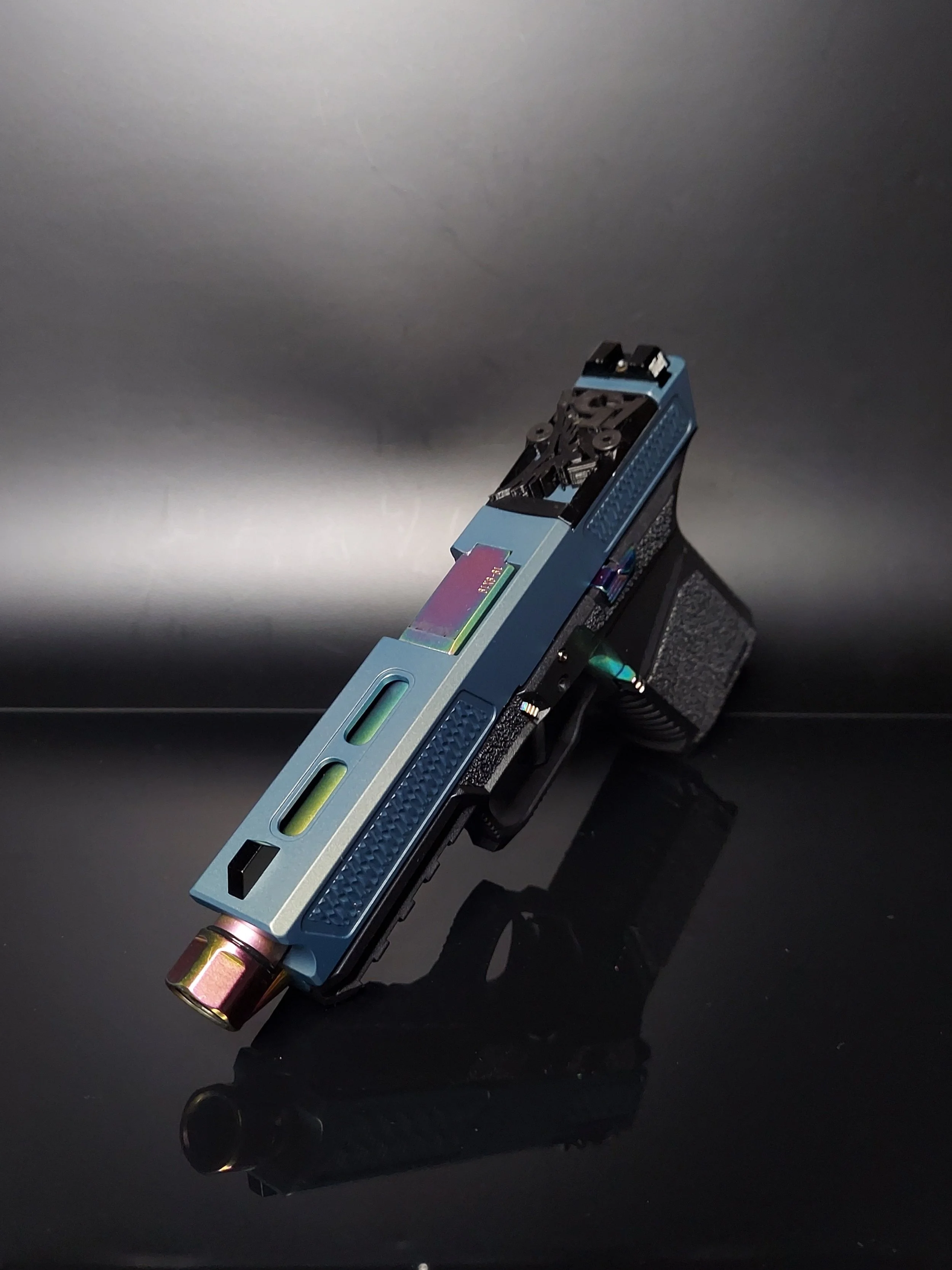 A semi-automatic handgun with a metallic blue slide and black grip, positioned on a dark reflective surface with a plain gray background.
