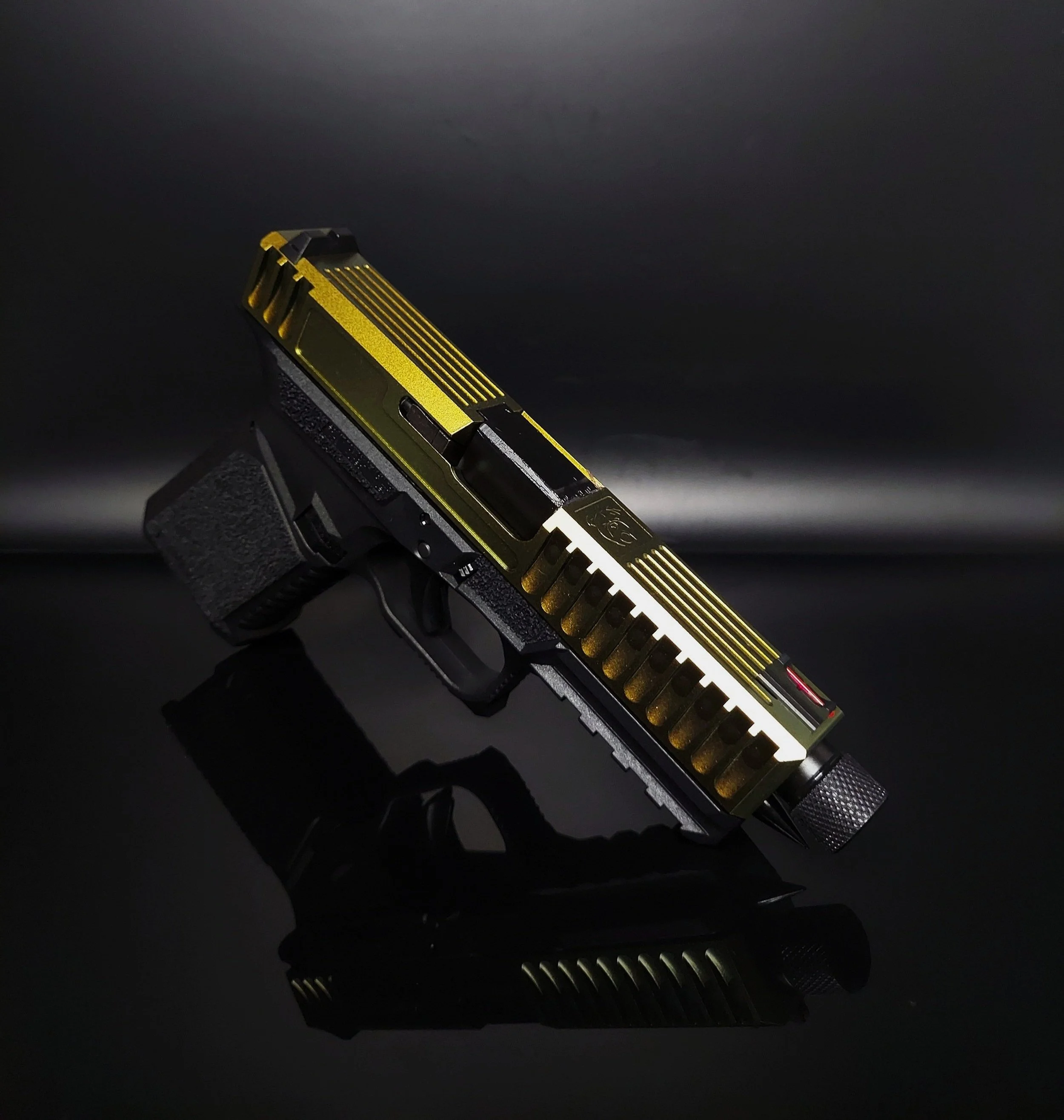 A black and gold semi-automatic pistol with a textured grip, placed on a black reflective surface against a black background.