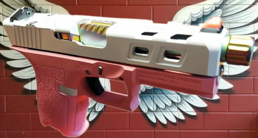 A pink and white handgun with a colorful slide, mounted against a wall with a wing emblem.