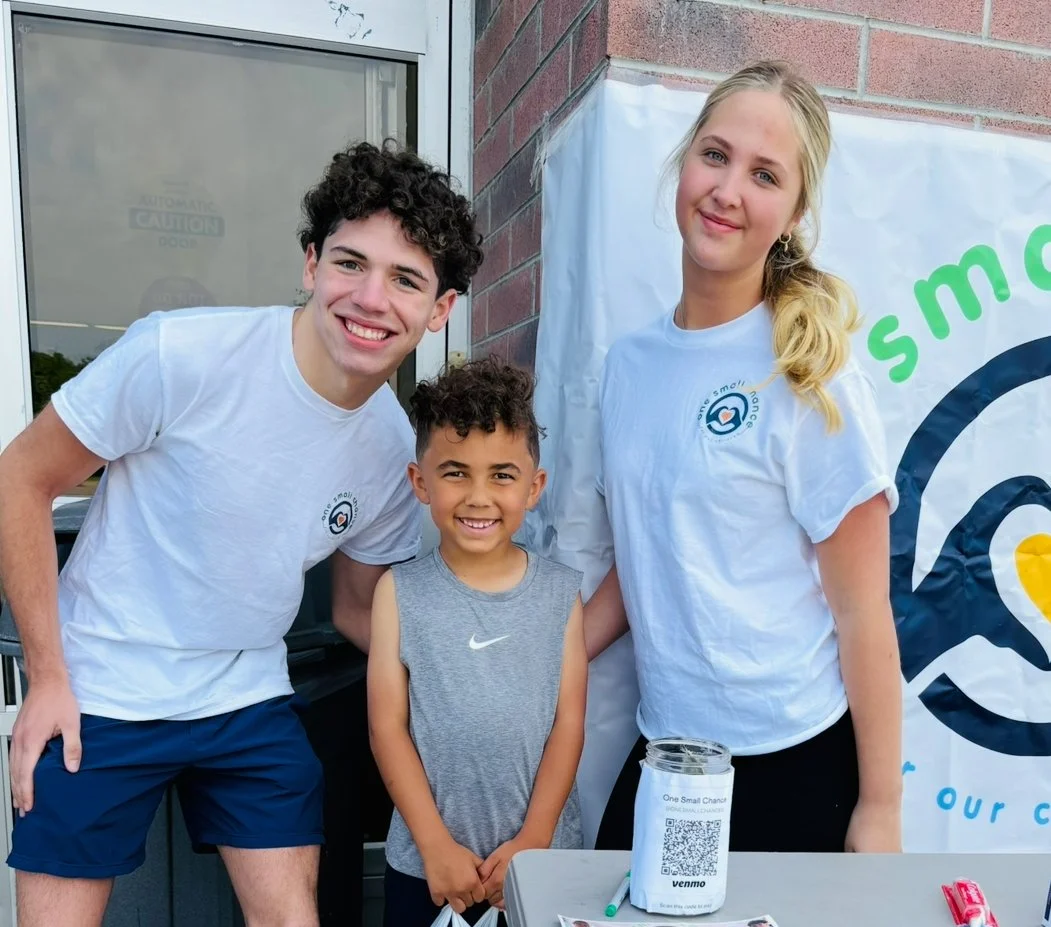 Volunteers in One Small Chance t-shirts smiling at an outdoor donation event
