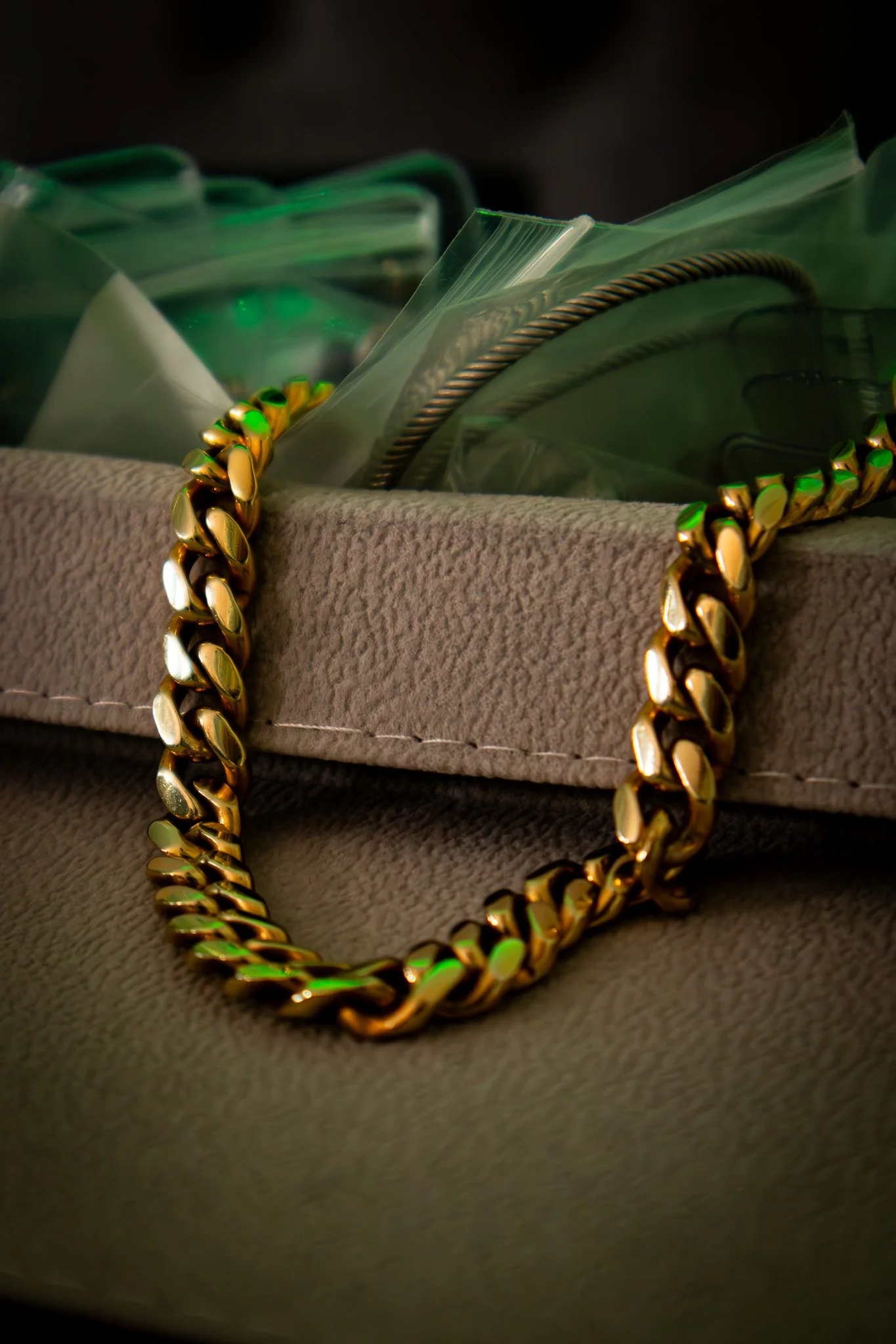 Close-up of a gold chain necklace resting on a beige textured surface with a plastic container in the background.