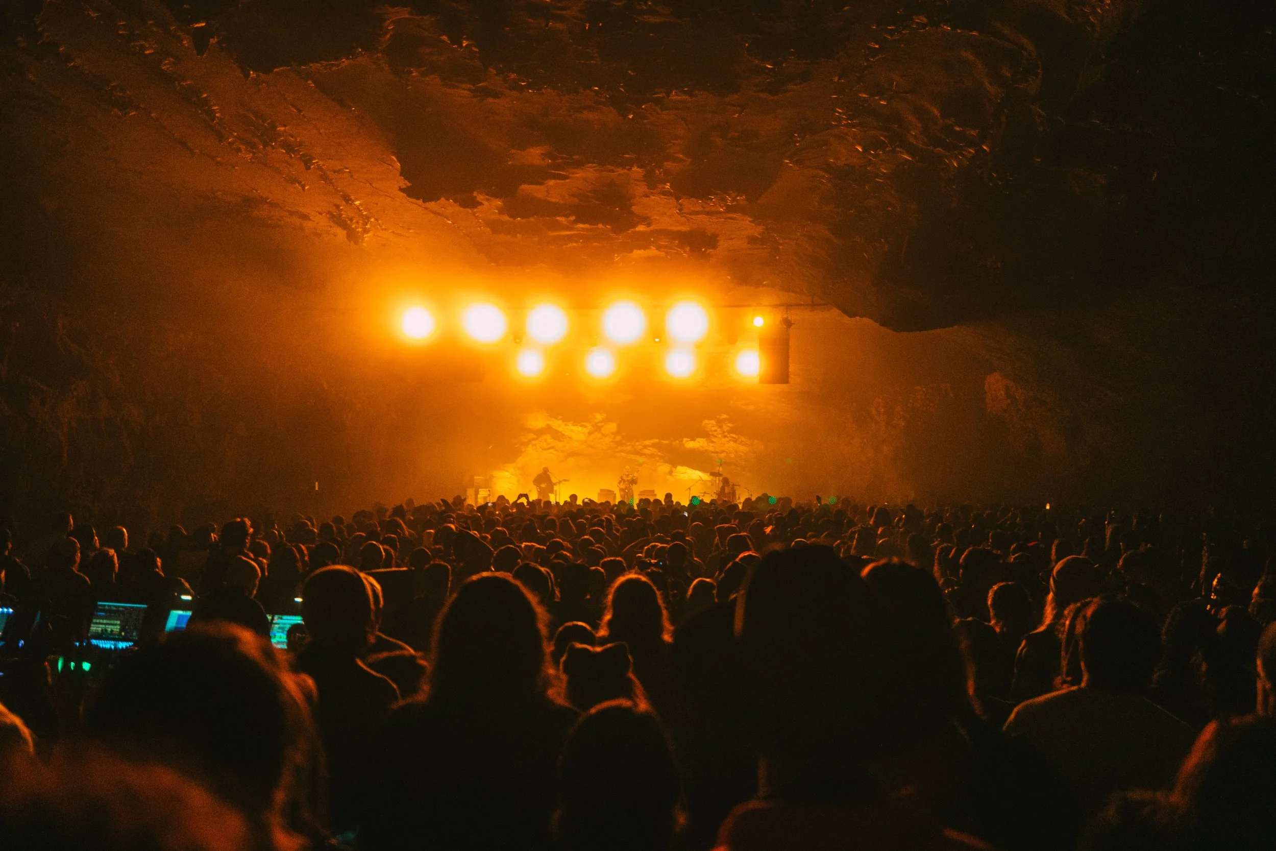 Concert inside a cave with bright stage lights and a large crowd of people.