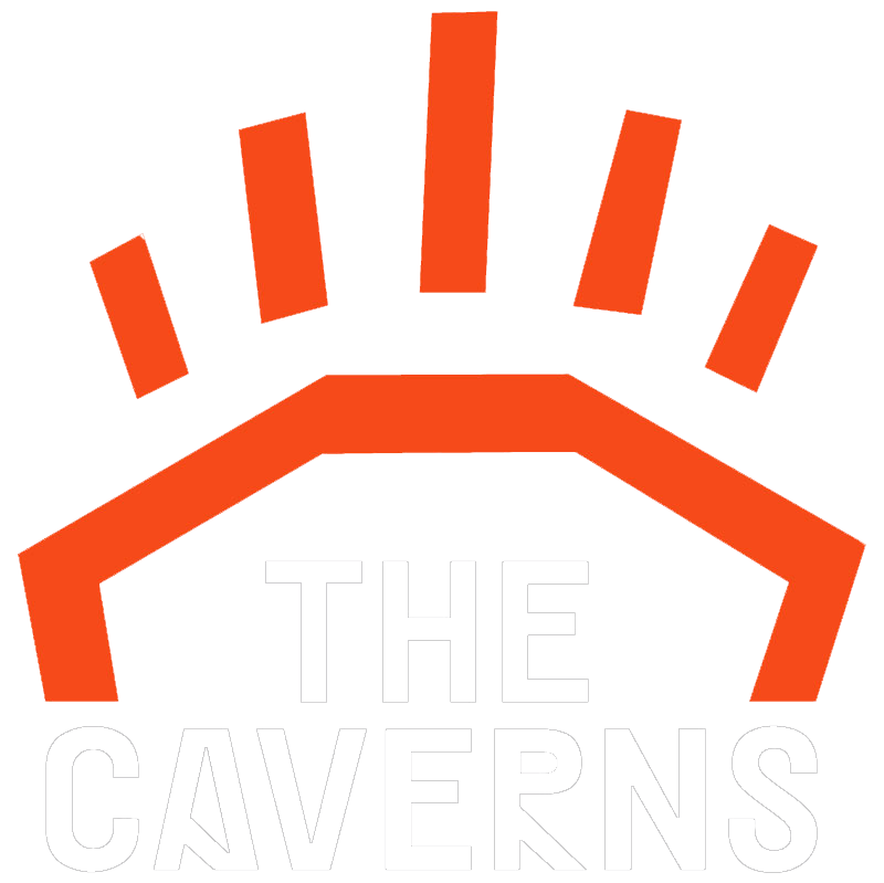 Logo for The Caverns featuring an orange stylized cavern entrance and upward pointing orange bars above it with white text reading "THE CAVERNS" below.