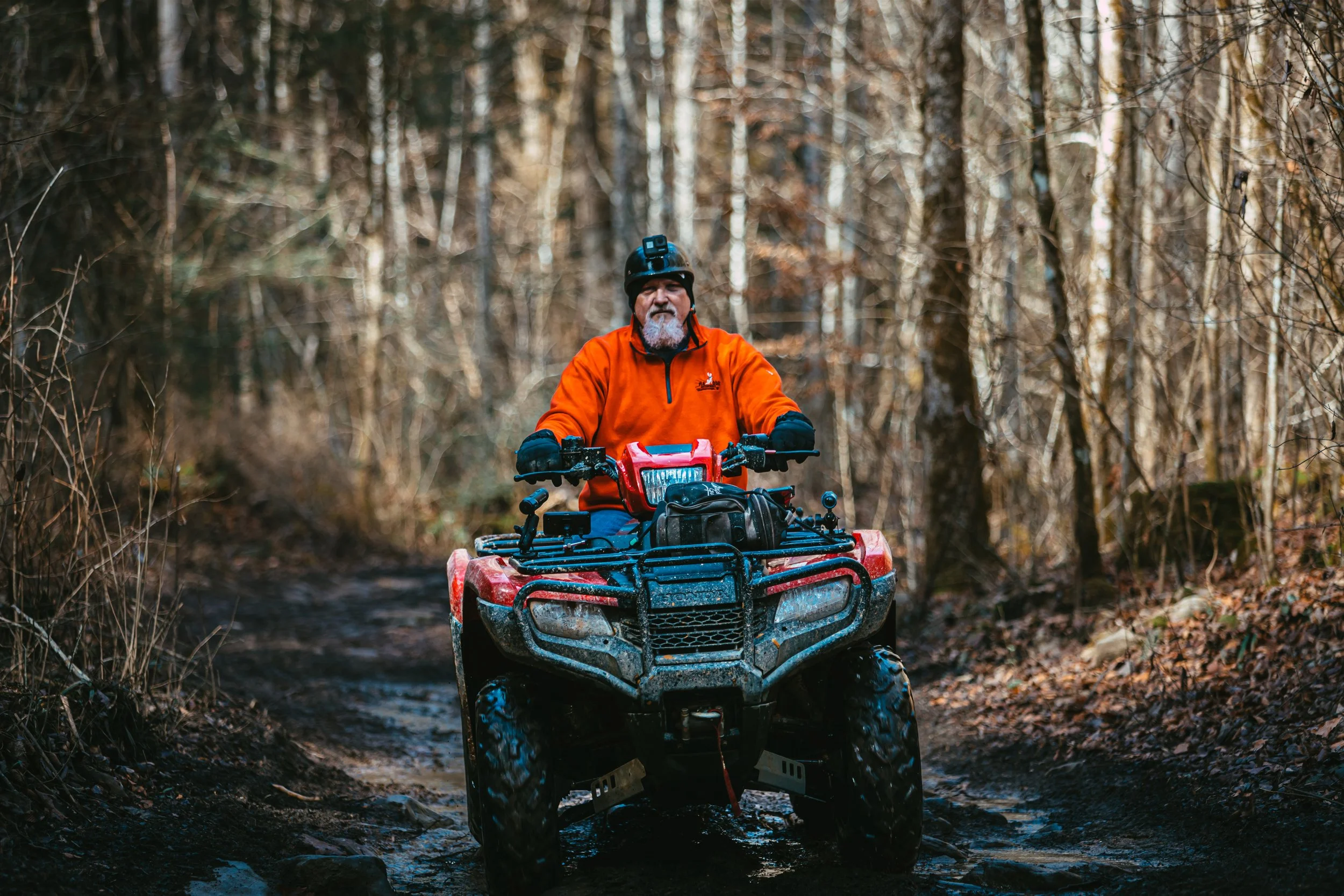 A man riding a red ATV through a muddy forest trail at Coalmont OHV Park in Grundy County, Tennessee.