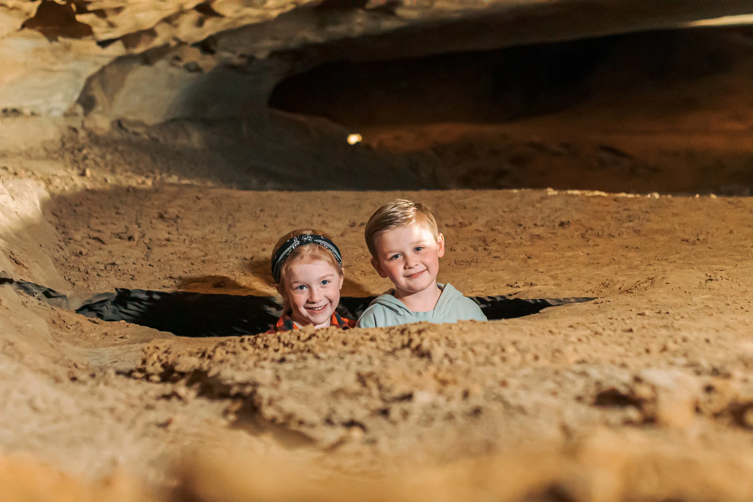 Two children look out from a hole in the ground inside Bigroom Cave at The Caverns in Pelham, TN.
