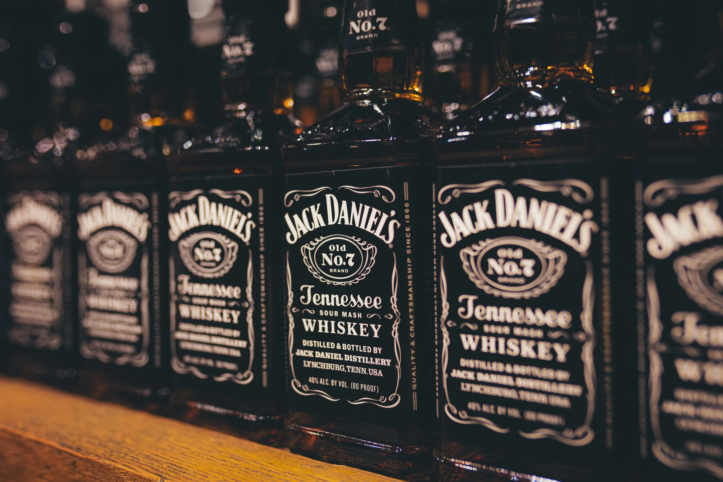Row of Jack Daniel's Tennessee Sour Mash Whiskey bottles on a wooden shelf.