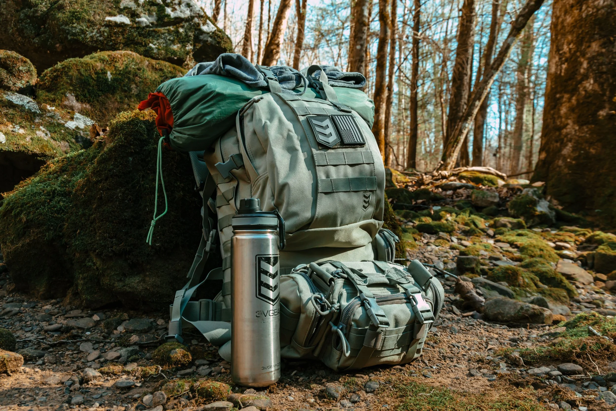 A backpack with a water bottle and gear on a forest ground.