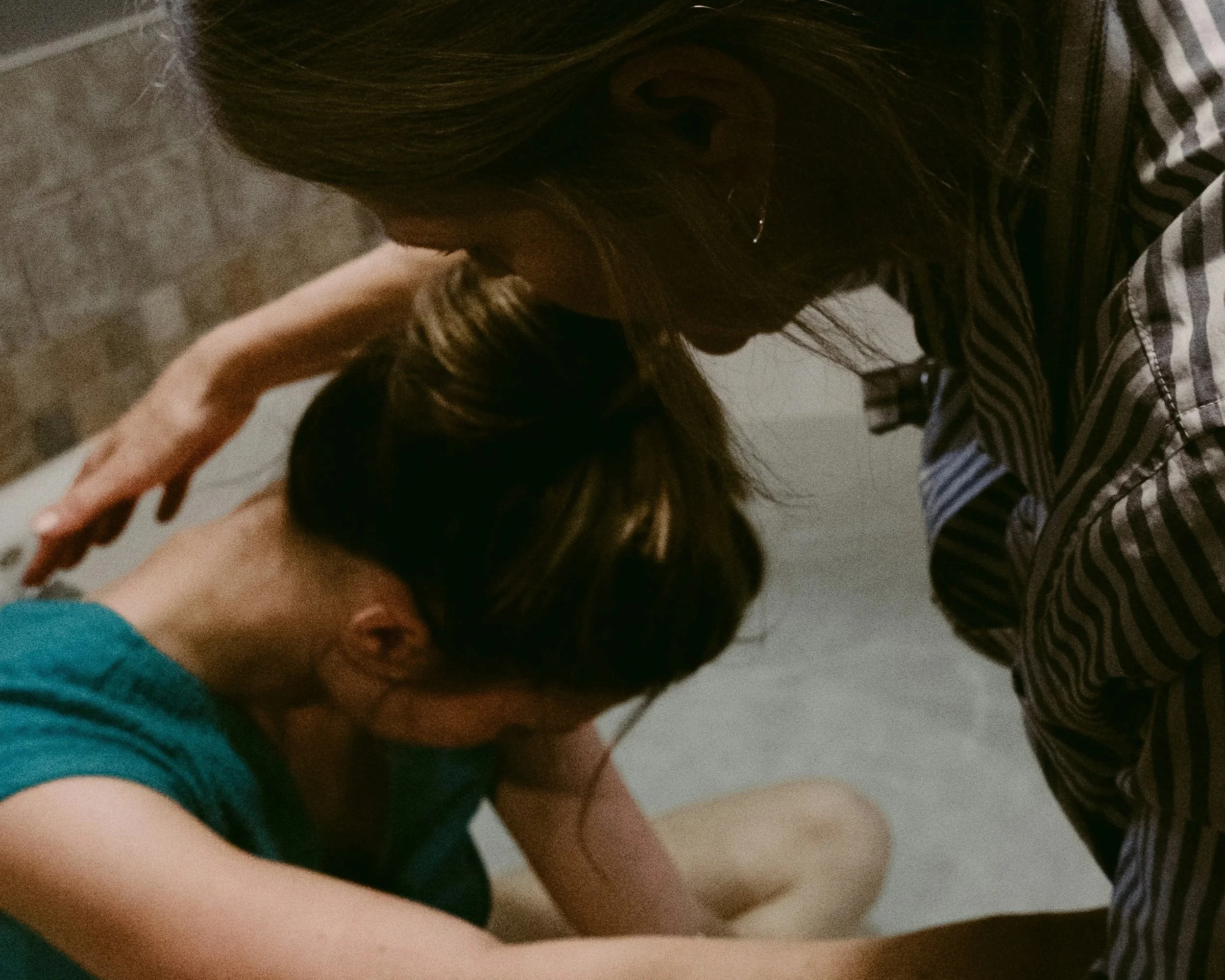 Close-up of two women with long hair, one in a striped shirt and the other in a blue shirt, appearing to be in a moment of gentle doula support.