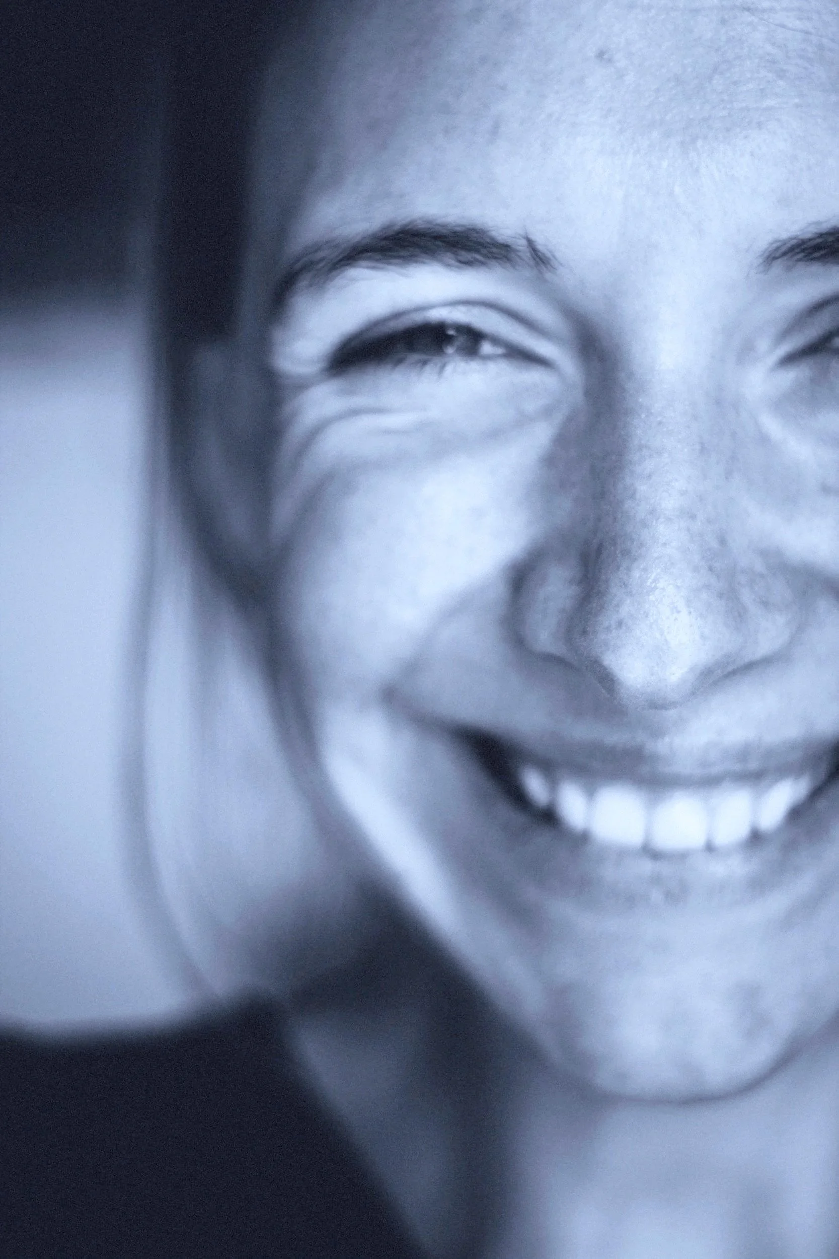 Close-up of a woman smiling in black and white, showing her teeth and dimples.