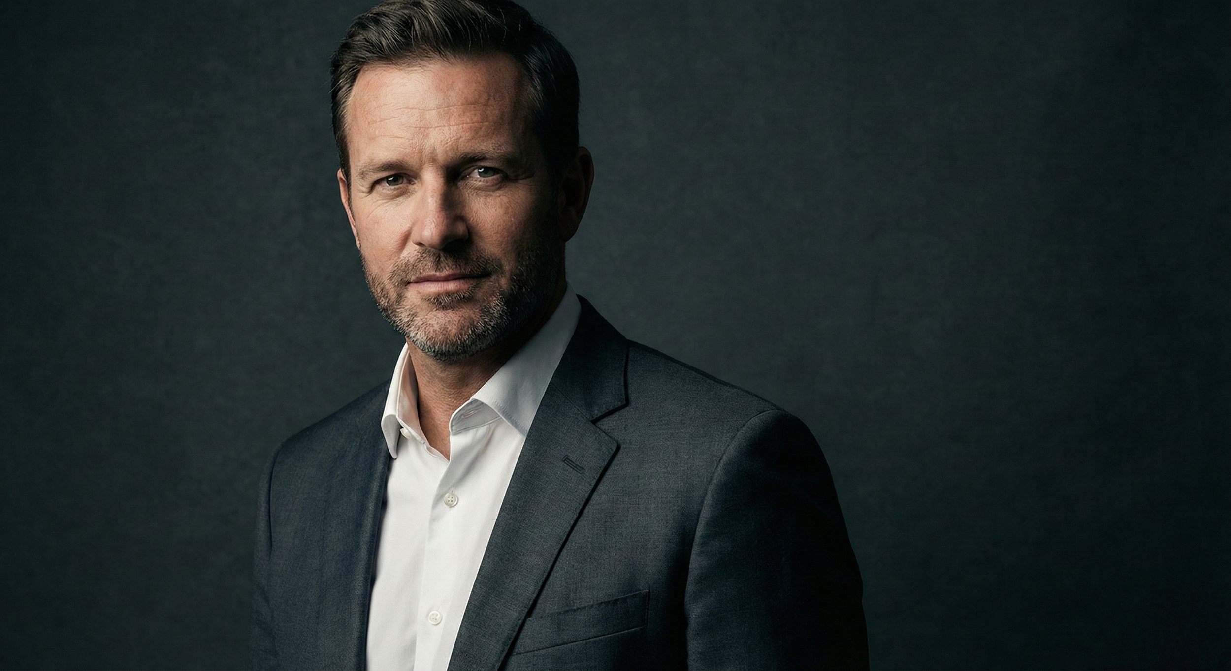 A modern corporate headshot of a male executive against a dark grey background, illustrating the 2026 trend of cinematic lighting and texture for NYC business teams.