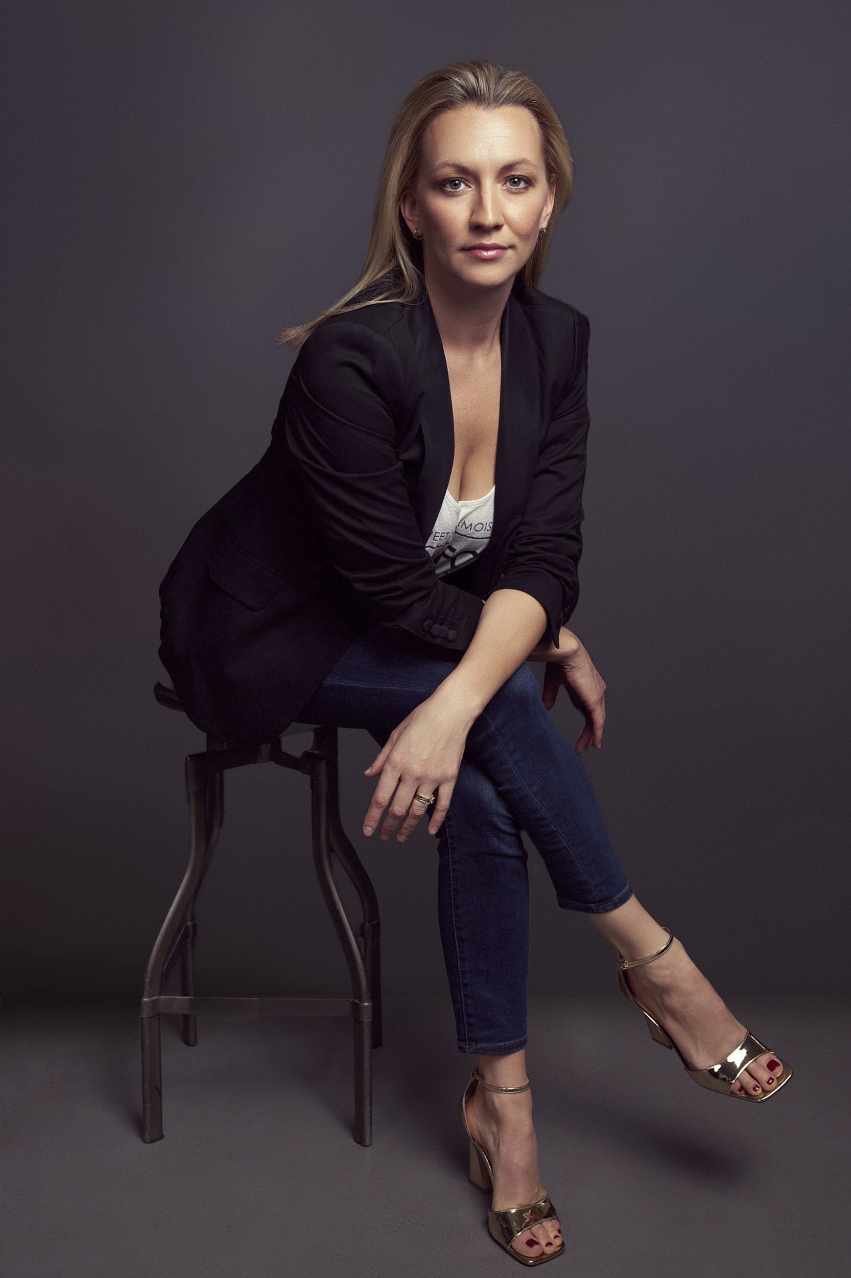 Female executive portrait in black blazer, seated pose, professional studio lighting, dark background.