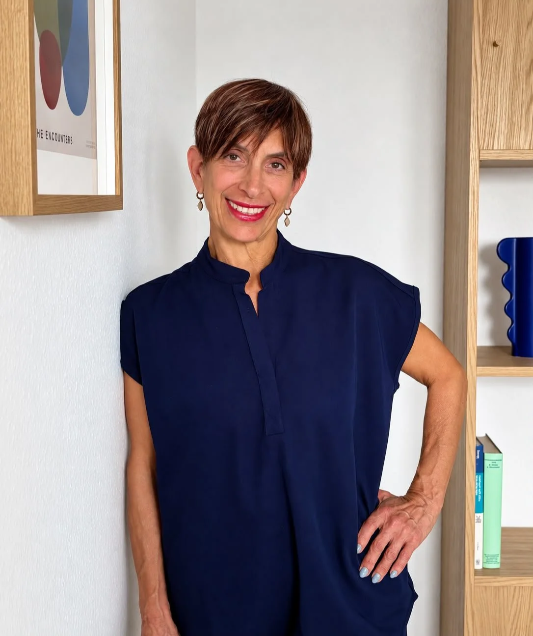 Heilpraktikerin Erika Makris lächelt in die Kamera und lehnt an der Wand.