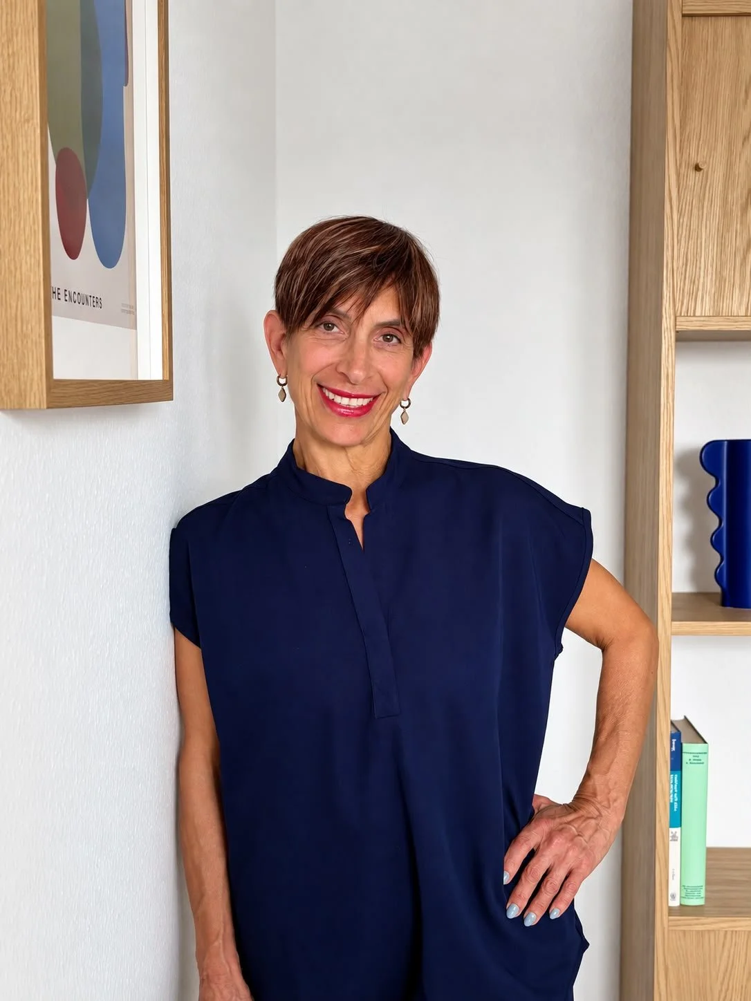 Porträt der Heilpraktikerin Erika Makris in ihrer Naturheilpraxis in Rödermark. Die Praxisinhaberin steht lächelnd vor einer hellen Wand mit modernen Einrichtungselementen.