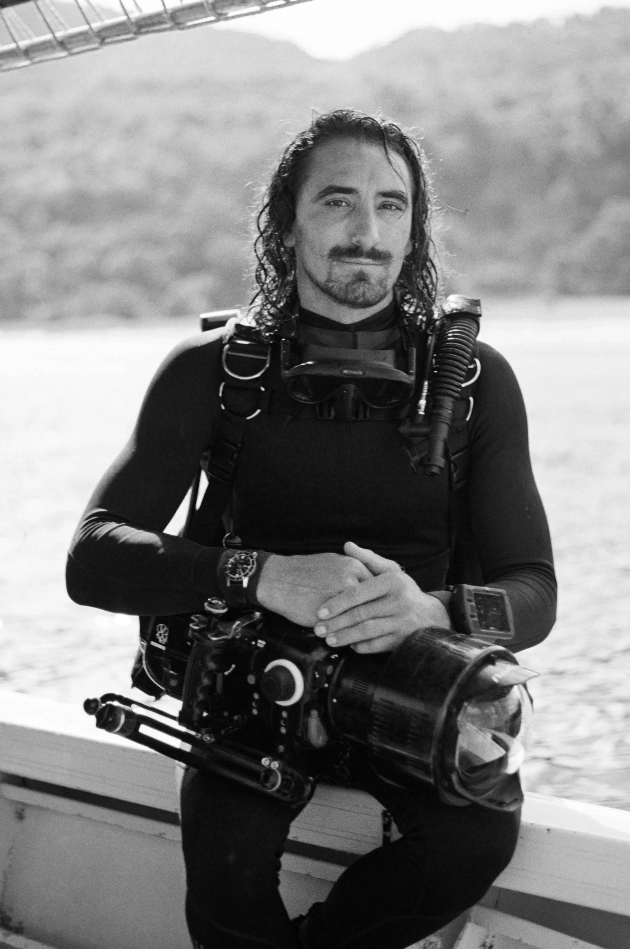 Kyle Roepke Black and white image of a scuba diver holding an underwater camera on a boat.