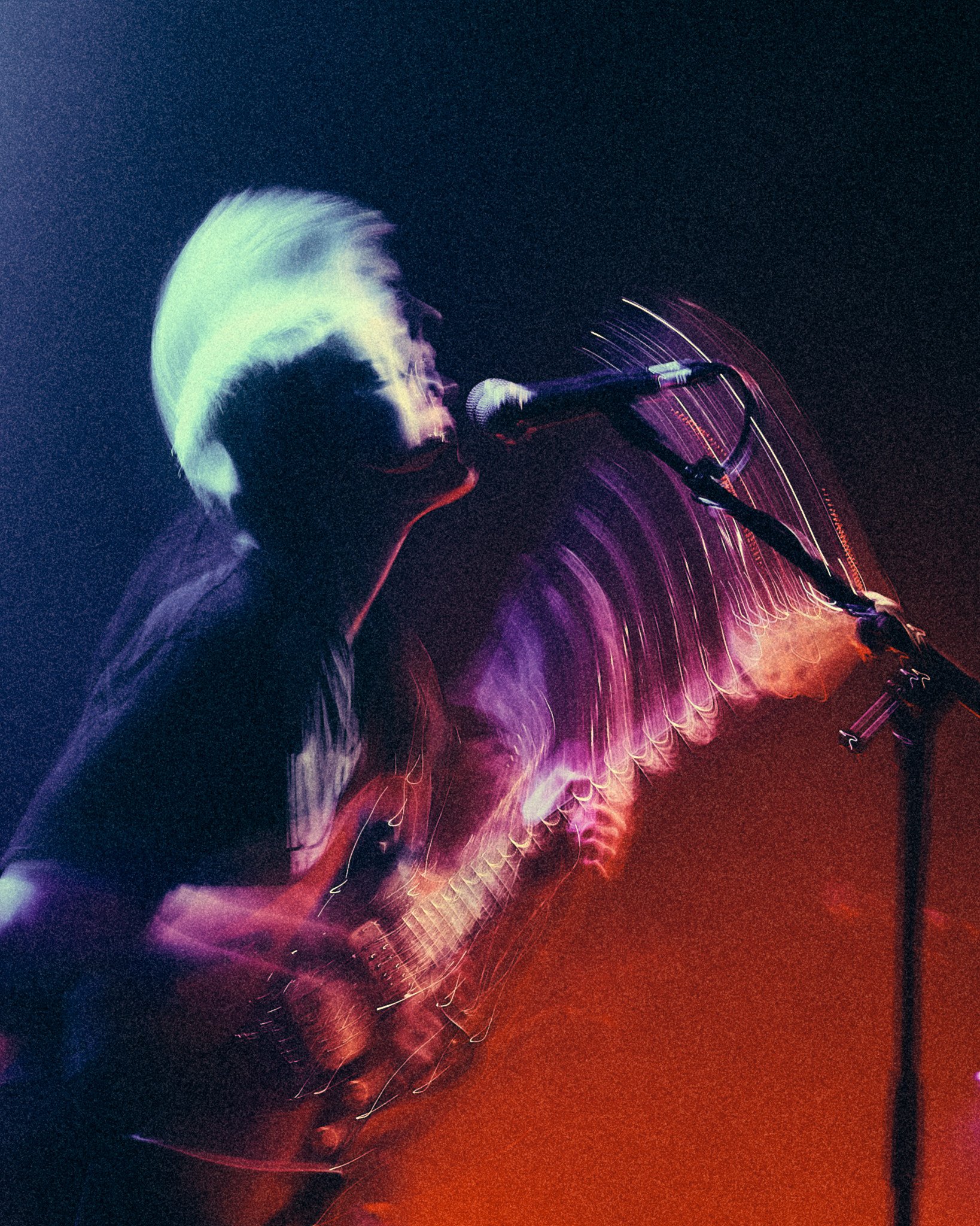 Musicien jouant d'une guitare électrique sur scène, avec des lumières colorées et un mouvement flou artistique.