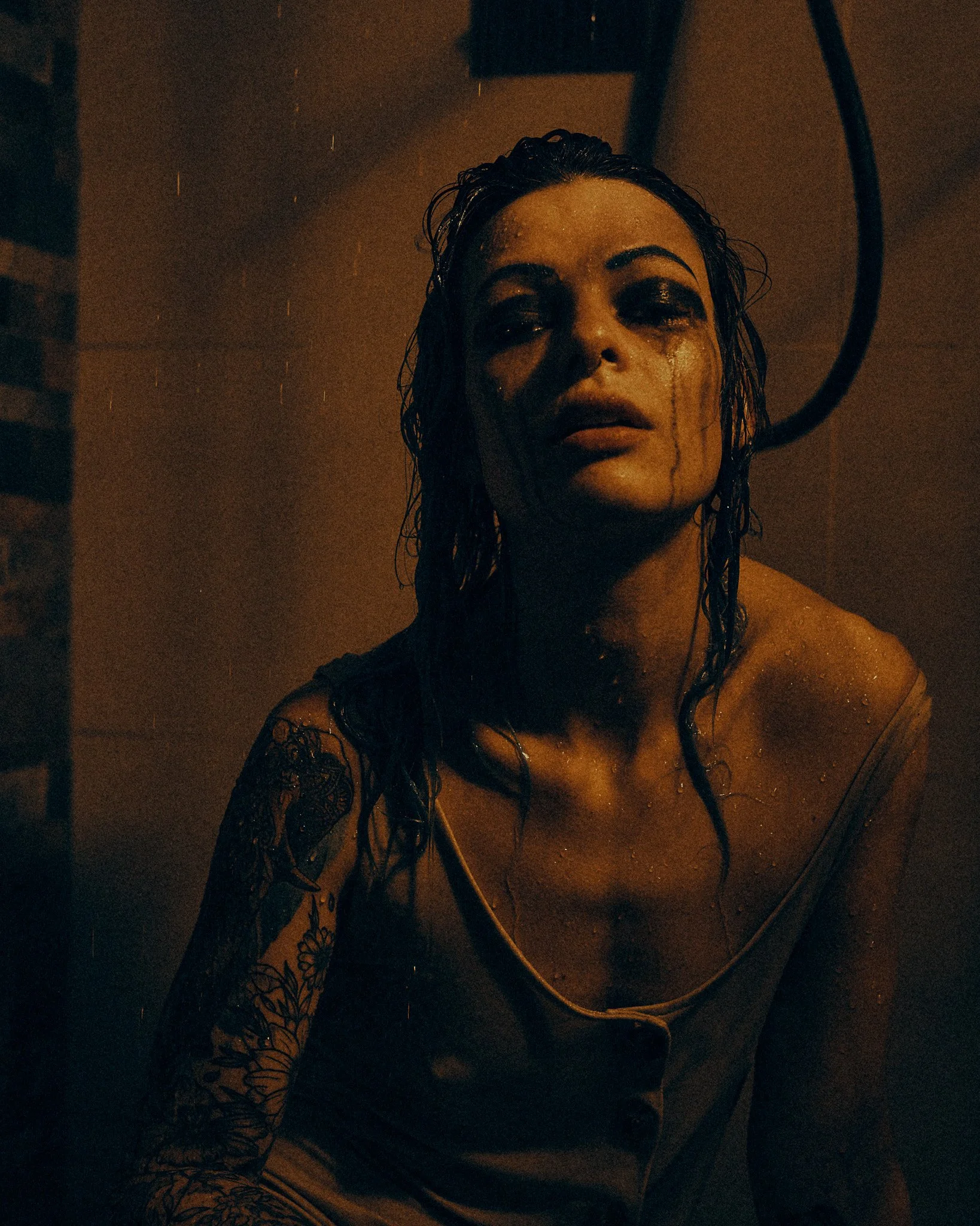 Une femme avec des cheveux mouillés, portant un chemisier, dans une pièce sombre, avec de l'eau sur son visage et son corps, un comportement triste ou mélancolique.