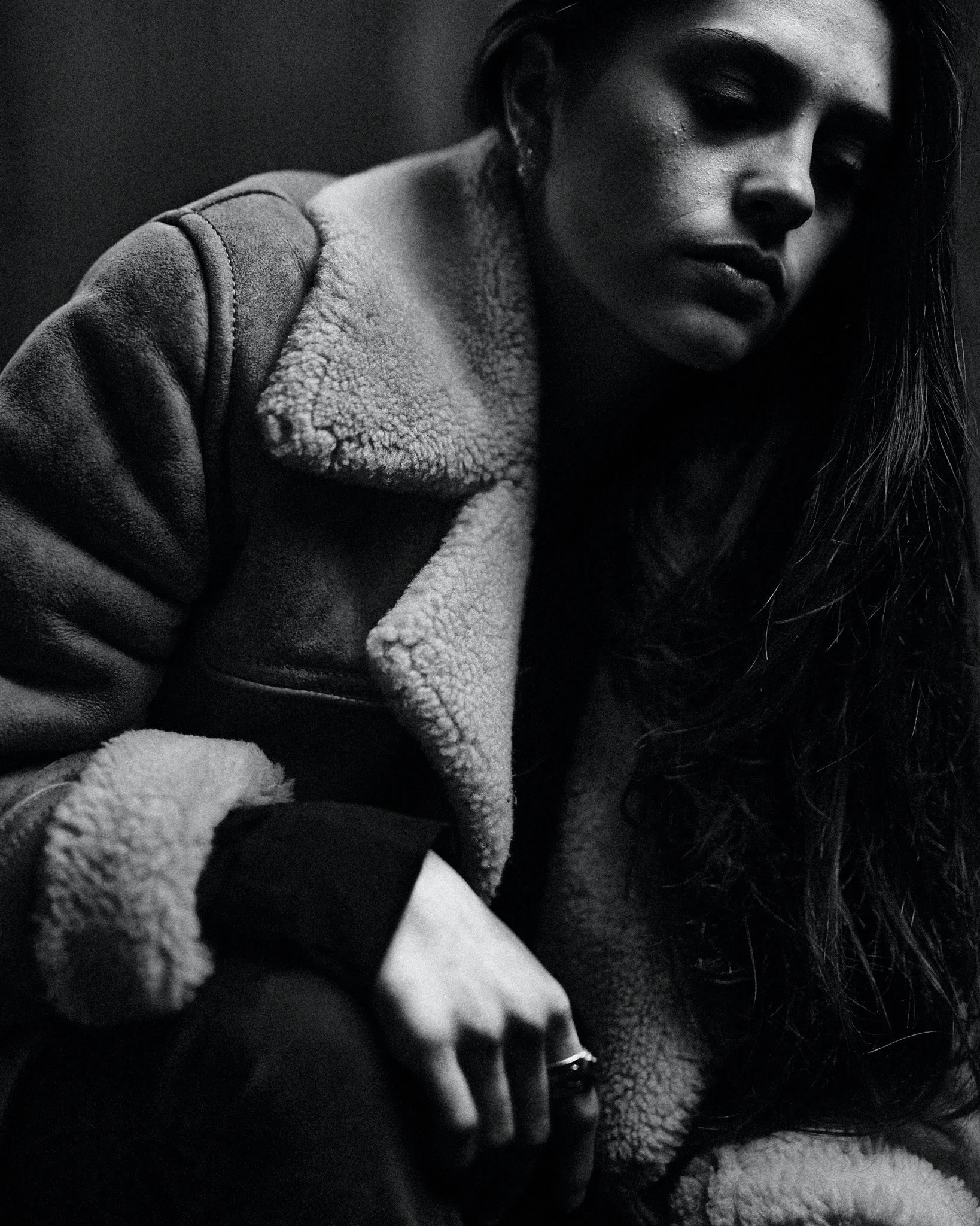 Femme en manteau en shearling, regard sombre, cheveux longs, en noir et blanc.