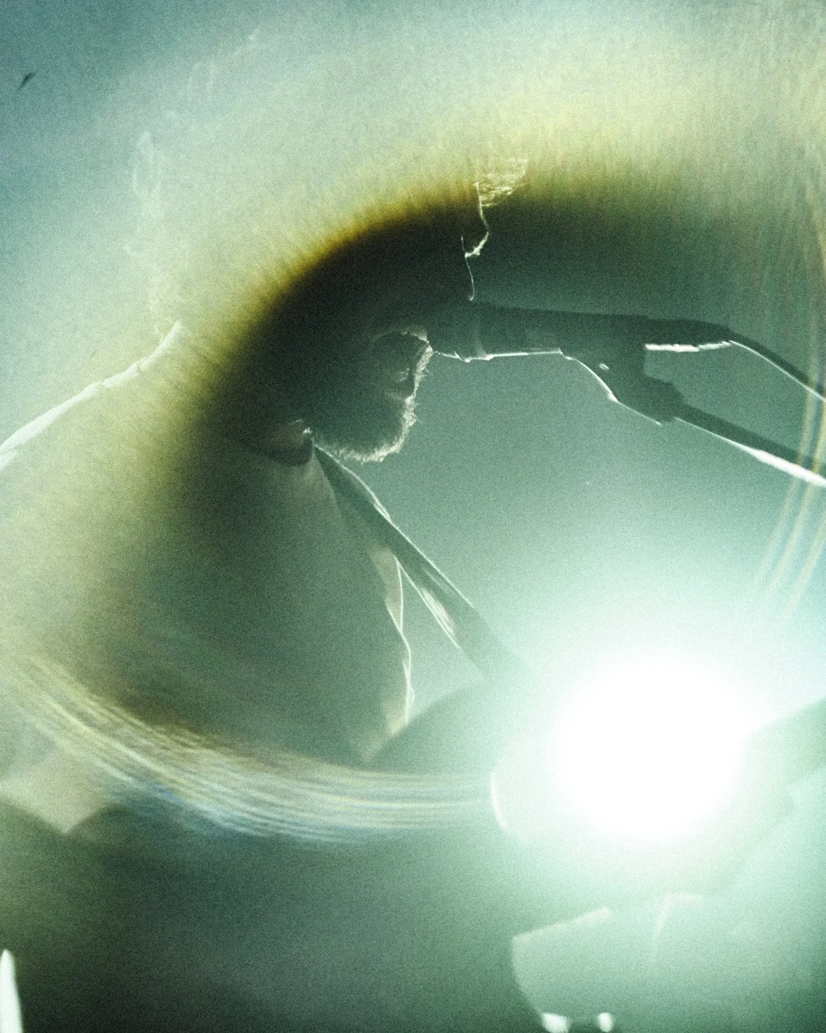 Une personne en train de jouer de la guitare sur scène, vue de profil avec une lumière brillante en arrière-plan.