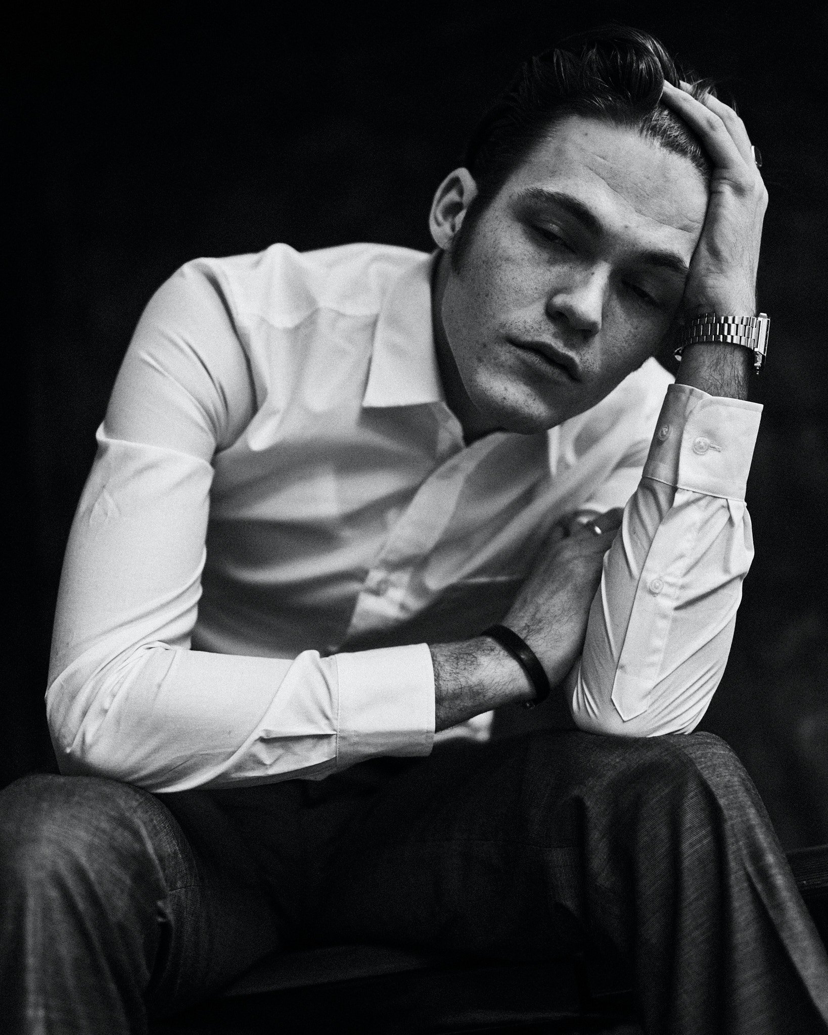 Jeune homme en chemise blanche, assis et posant avec sa main sur sa tête, regardant vers l'objectif dans un style noir et blanc.