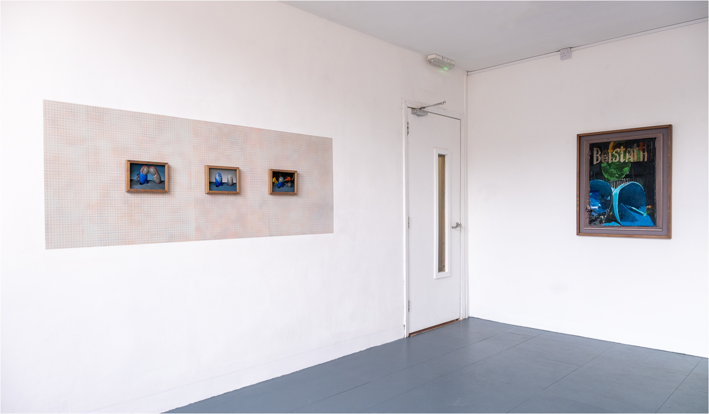 Art gallery with three framed pieces featuring colorful objects on the left wall and a larger framed piece with small scale paintings on the right wall + a mural, white walls, gray flooring, and a door with a narrow window.
