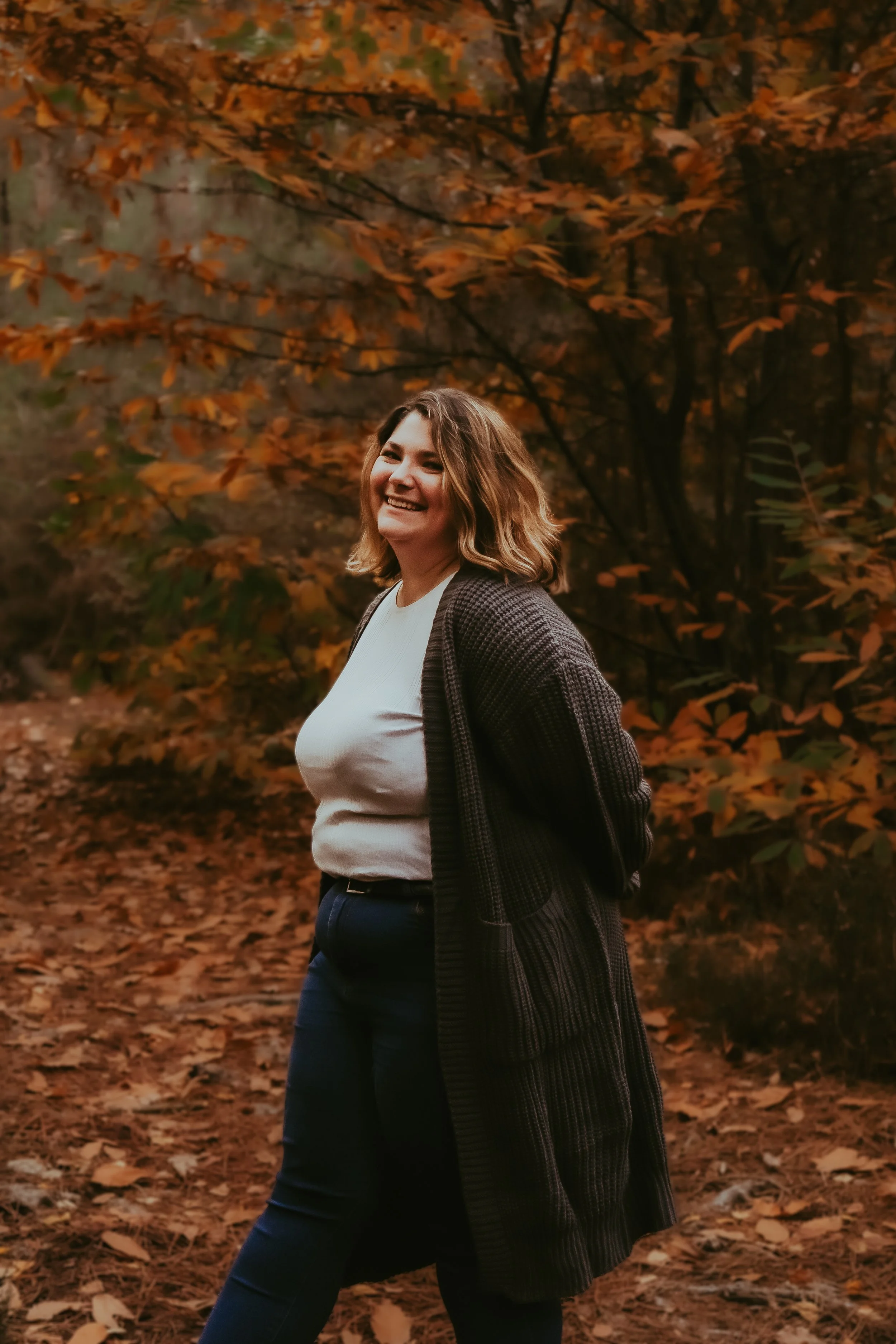 Une femme souriante dans une forêt aux couleurs automnales.