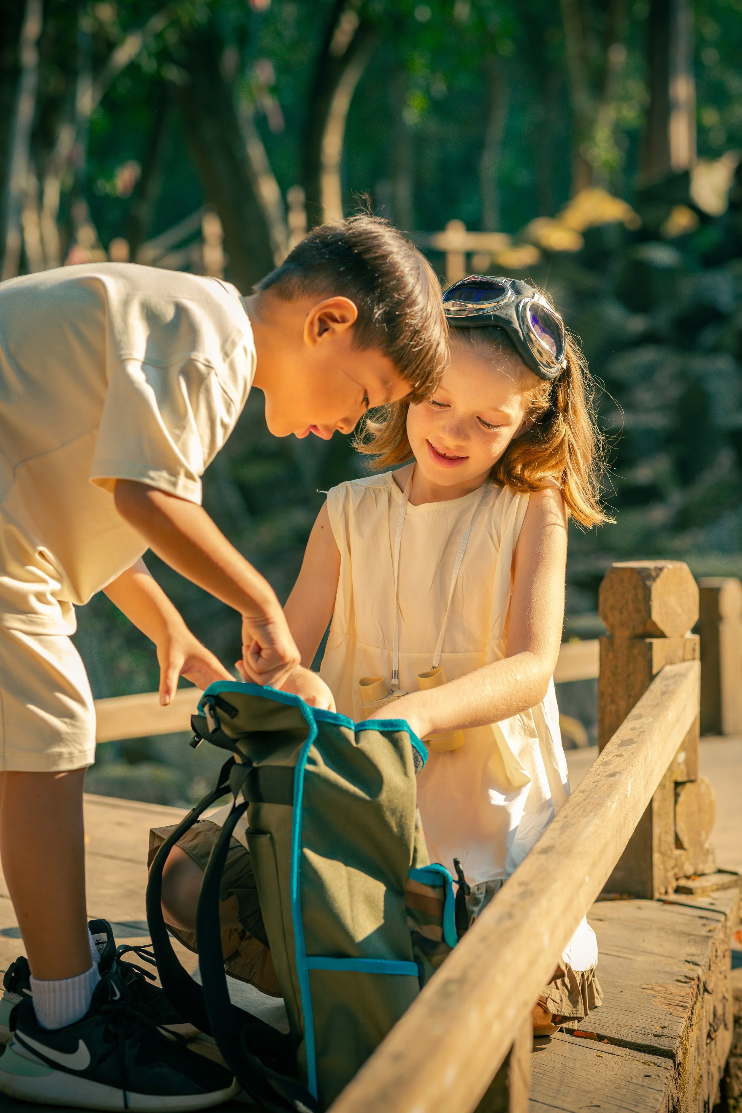 Two children looking into a backpack outdoors at Ta Prohm in Siem Reap, Cambodia.