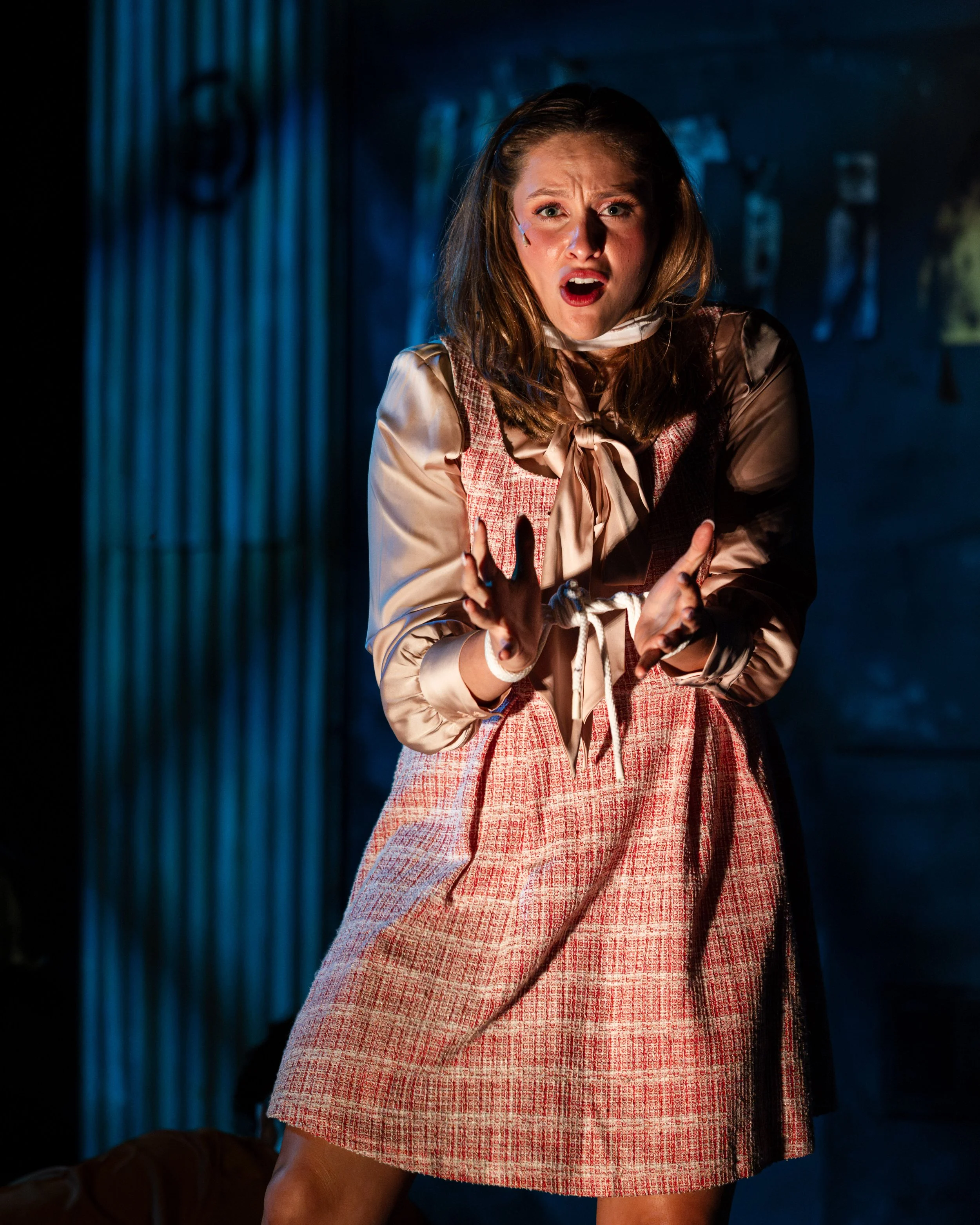 Hope Cladwell sings with her hands raised, her face warmly lit against a deep blue background, in Urinetown.