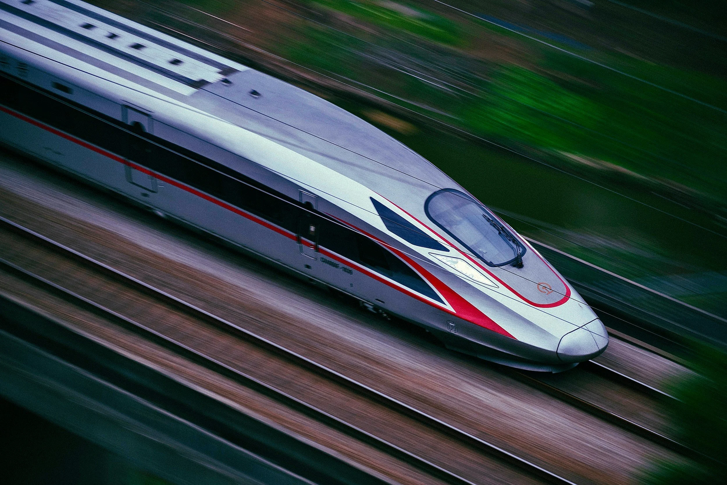 A high-speed train moving rapidly along train tracks on a green landscape background.