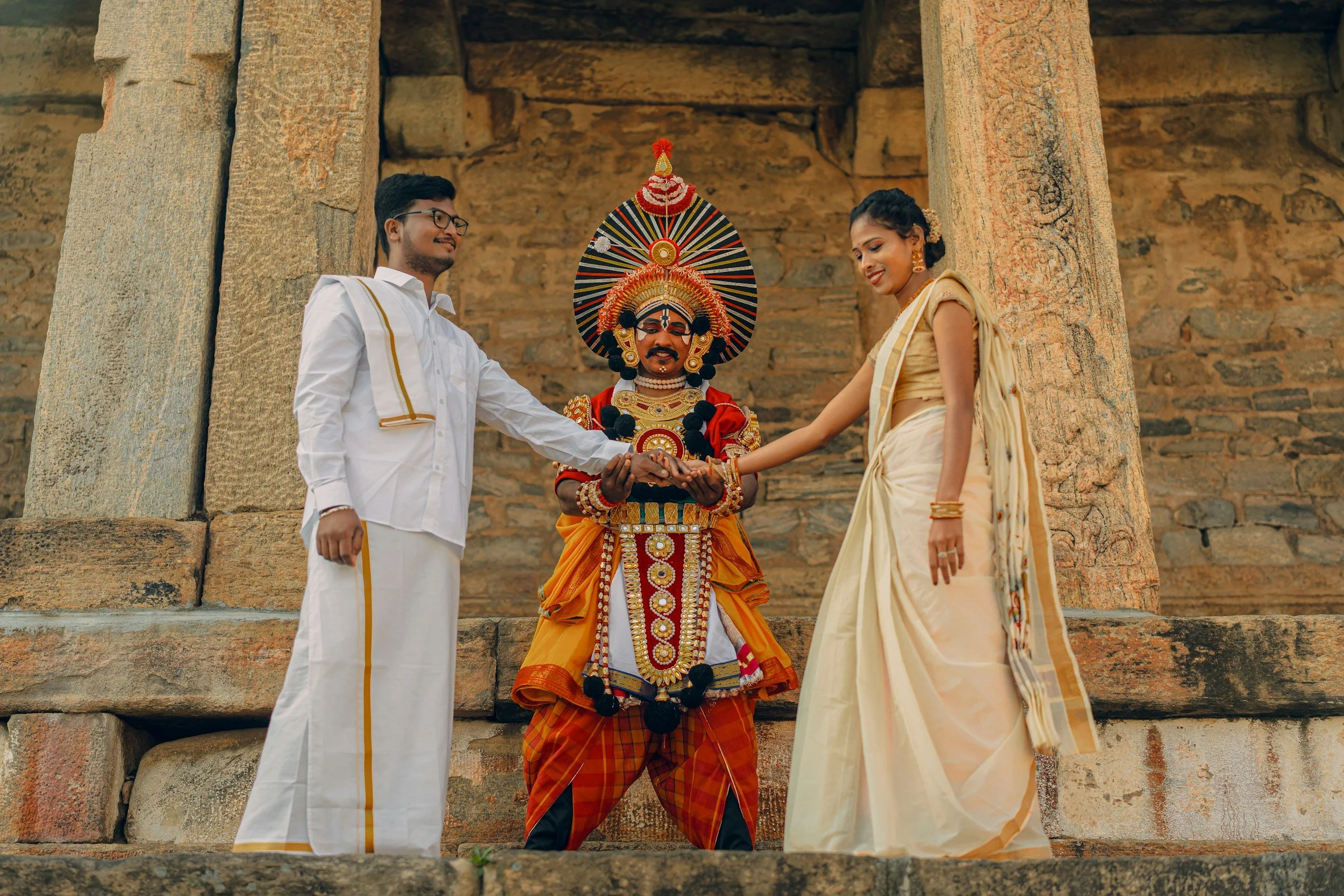 A couple performing a traditional Tamil wedding ceremony with decorated idol of a South Indian deity in the background.