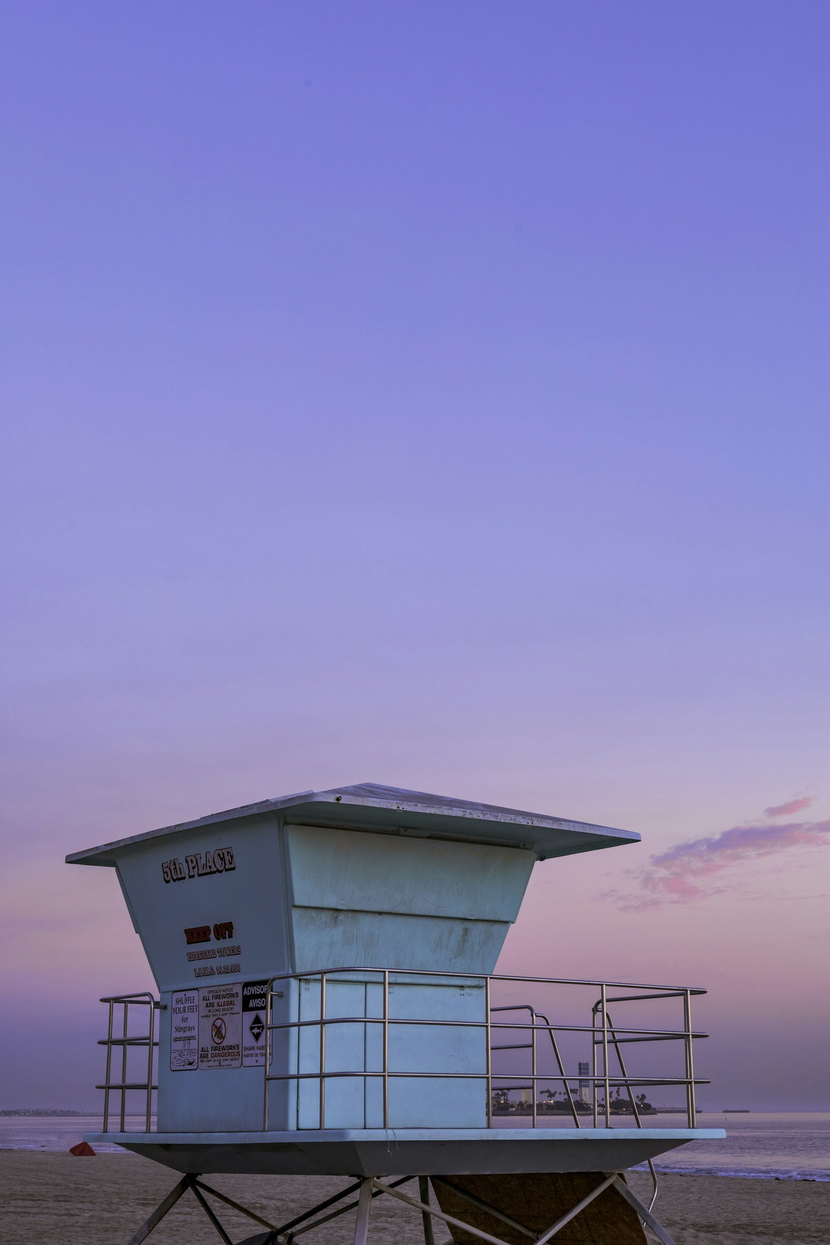 A lifeguard tower on a beach during sunset, with a purple and pink sky in the background.