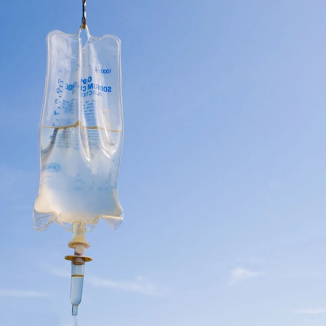An IV fluid bag hanging against a clear blue sky.