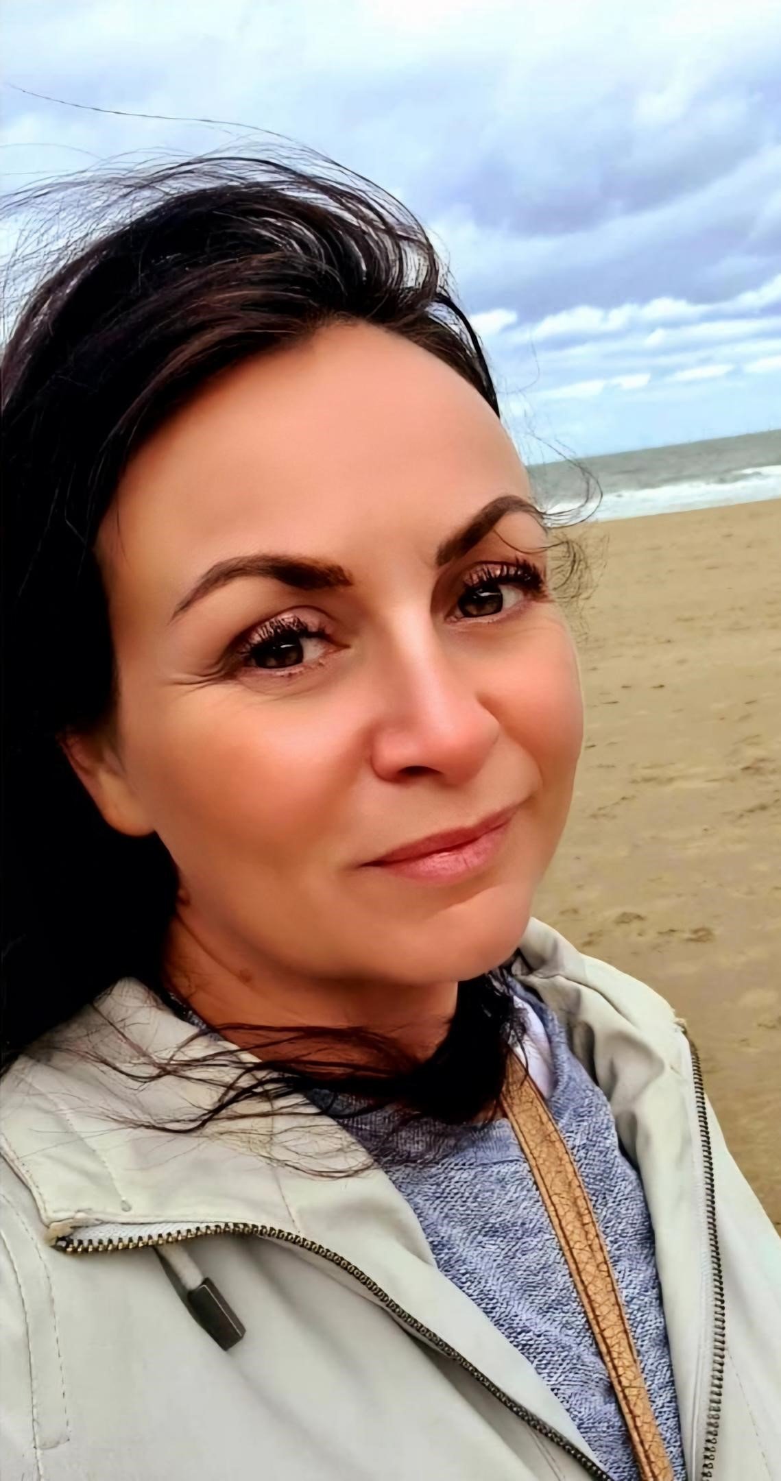 Woman smiling on a beach with cloudy skies.