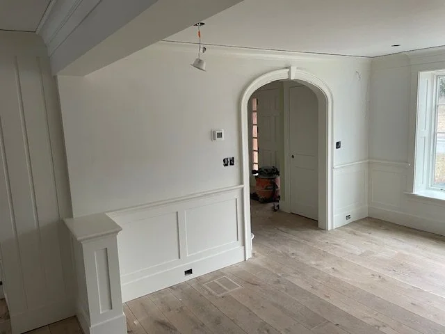 Home interior remodel with custom wainscoting, detailed trim work, arched doorway, and wide-plank hardwood floors completed by P Jordan Construction in New Hampshire.