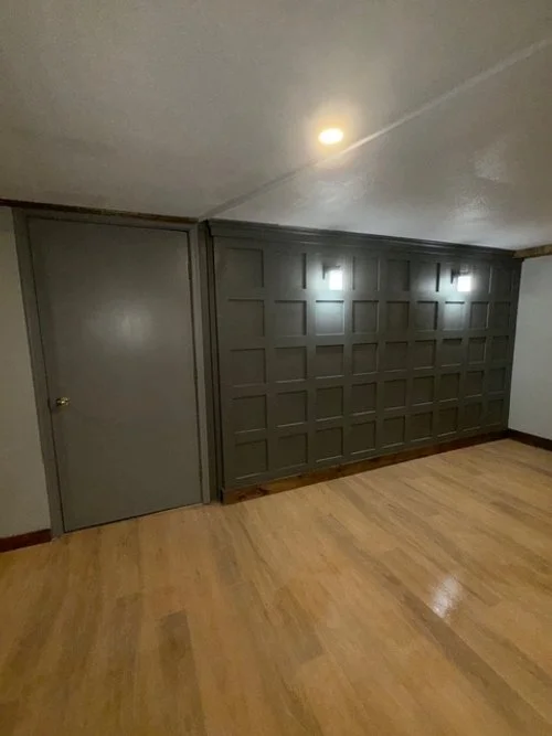 Empty room with gray door, wood floor, and a gray wall with a grid pattern and two wall-mounted lights.