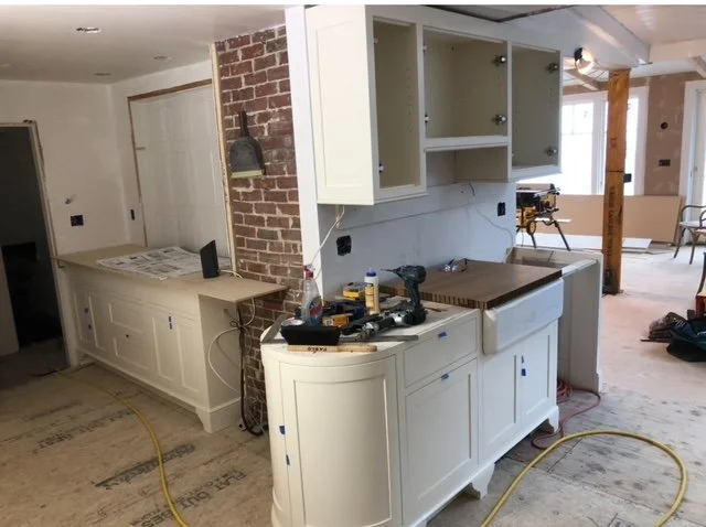 Kitchen remodel in progress featuring custom white cabinetry installation, exposed brick accent wall, farmhouse sink base, and detailed trim work by P Jordan Construction in New Hampshire