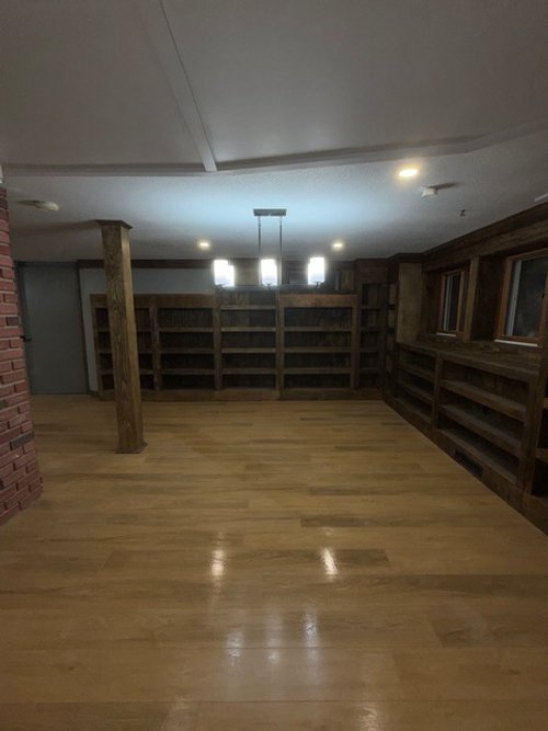 Empty room with wooden floors, built-in wooden shelves on the walls, windows, and a hanging light fixture.