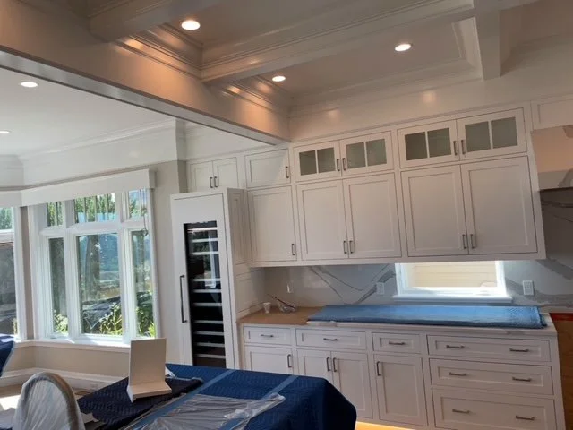 Completed kitchen remodel with custom white cabinetry, crown molding, glass-front uppers, and large windows providing natural light, built by P Jordan Construction in New Hampshire