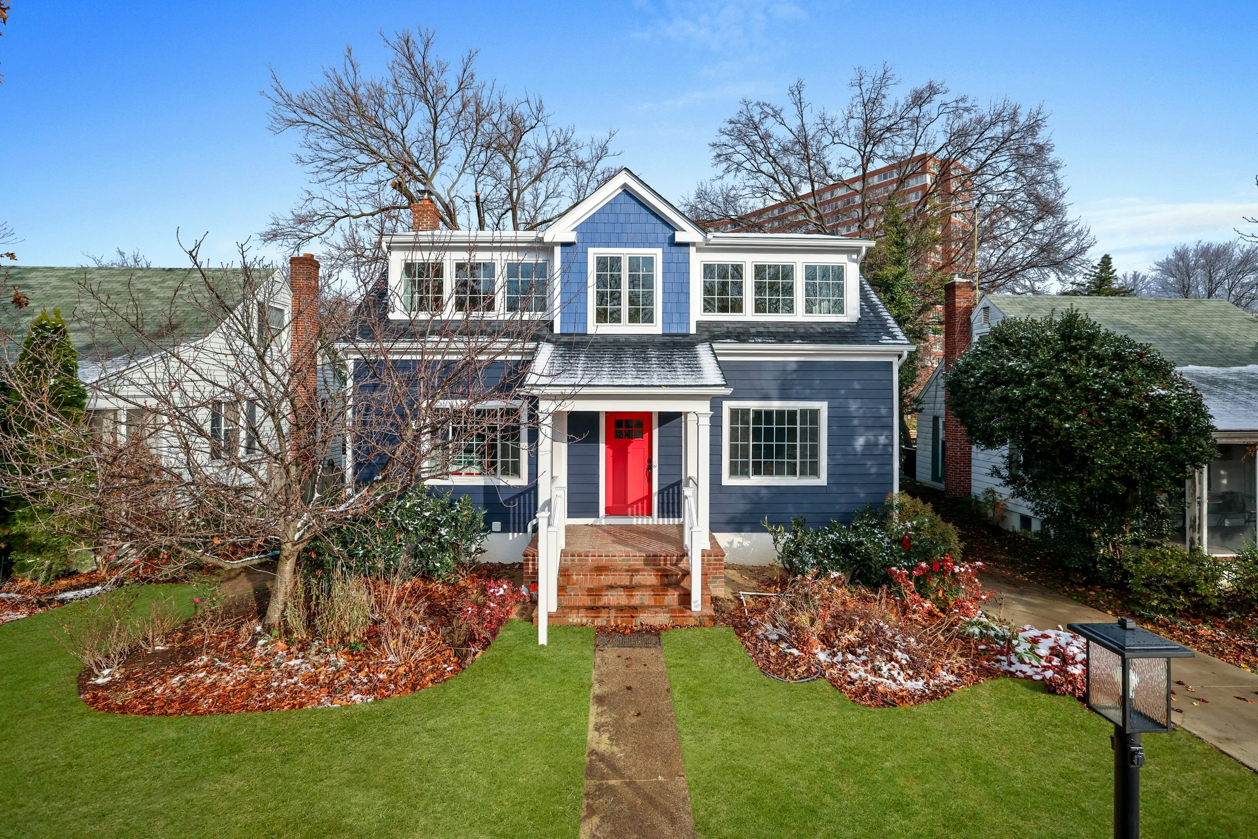 Front view of a two-story pop-top home renovation completed by G2 Builders with white trim, red front door, and brick steps. 