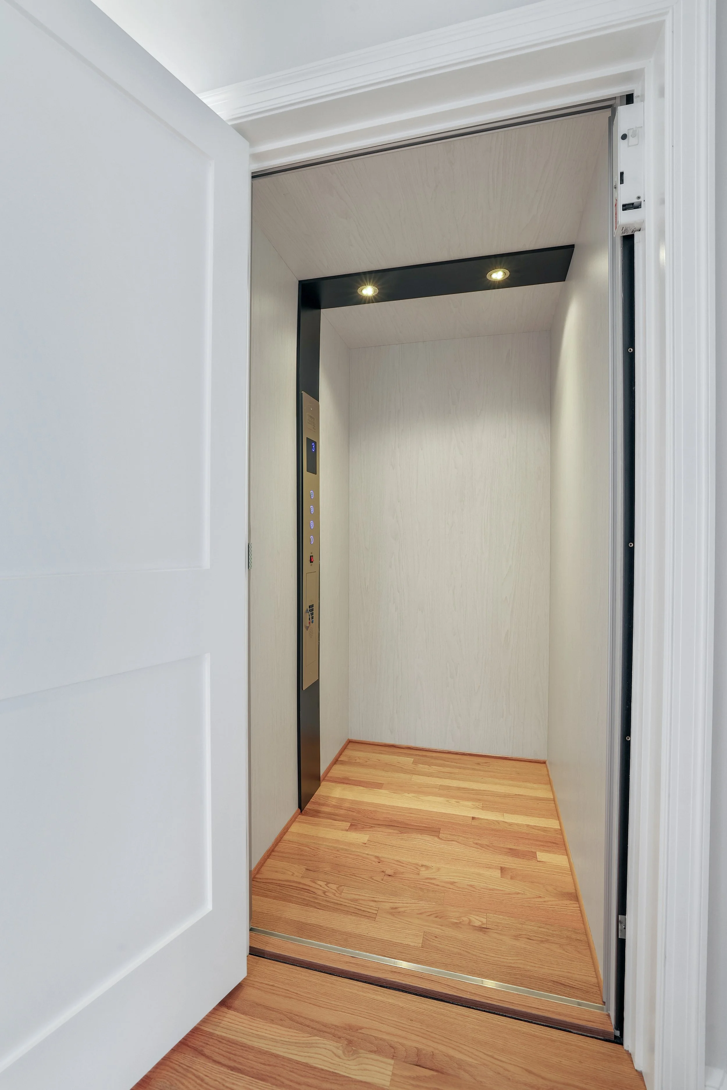 Empty modern elevator with closed doors, wooden flooring, and control panel with buttons on the side.