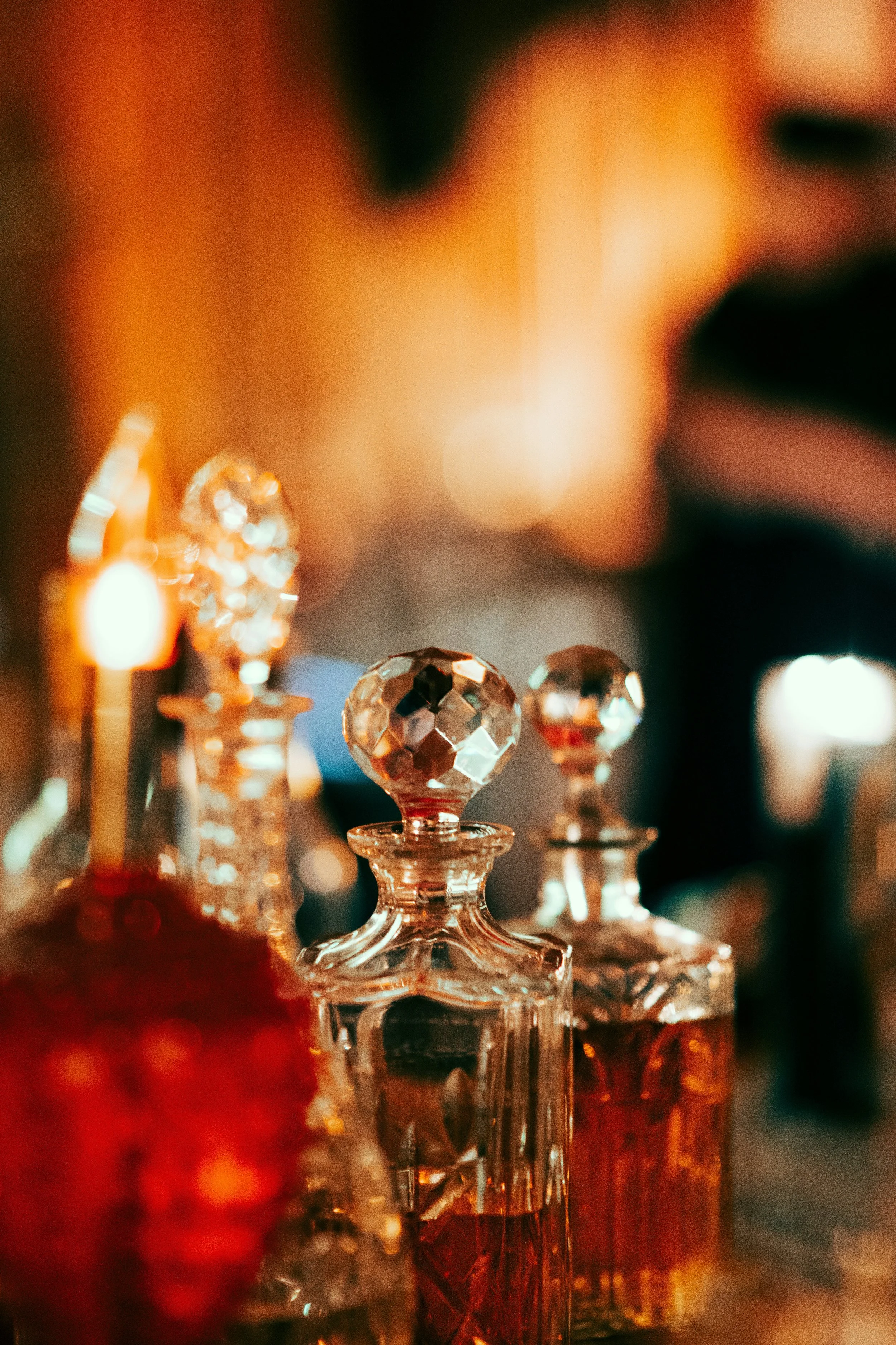 Close-up of ornate glass perfume bottles with faceted stoppers, illuminated by warm ambient lighting.