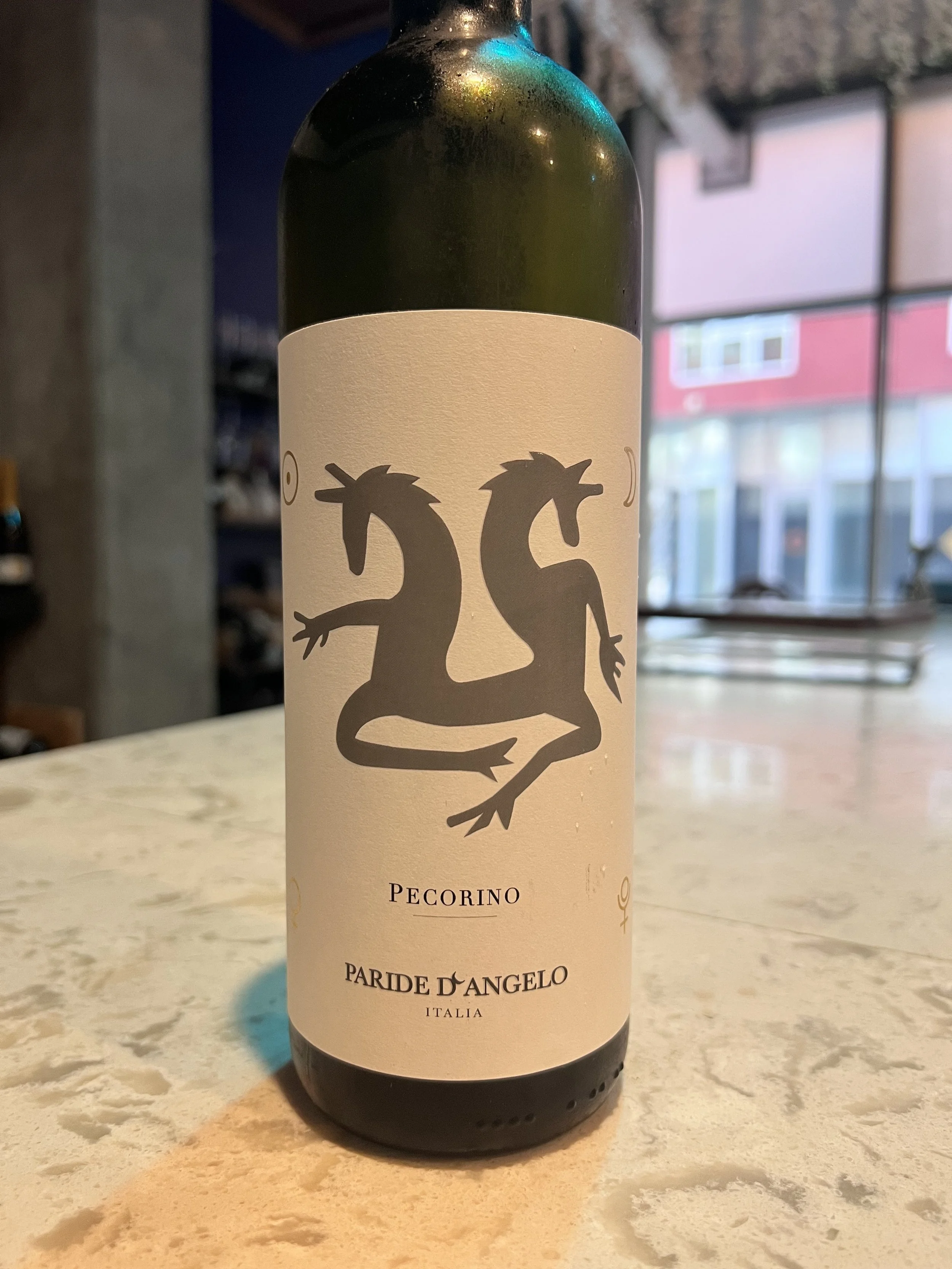 A bottle of Pecorino Paride D'Angelo white wine from Italy on a marble counter, with a scenic window background.