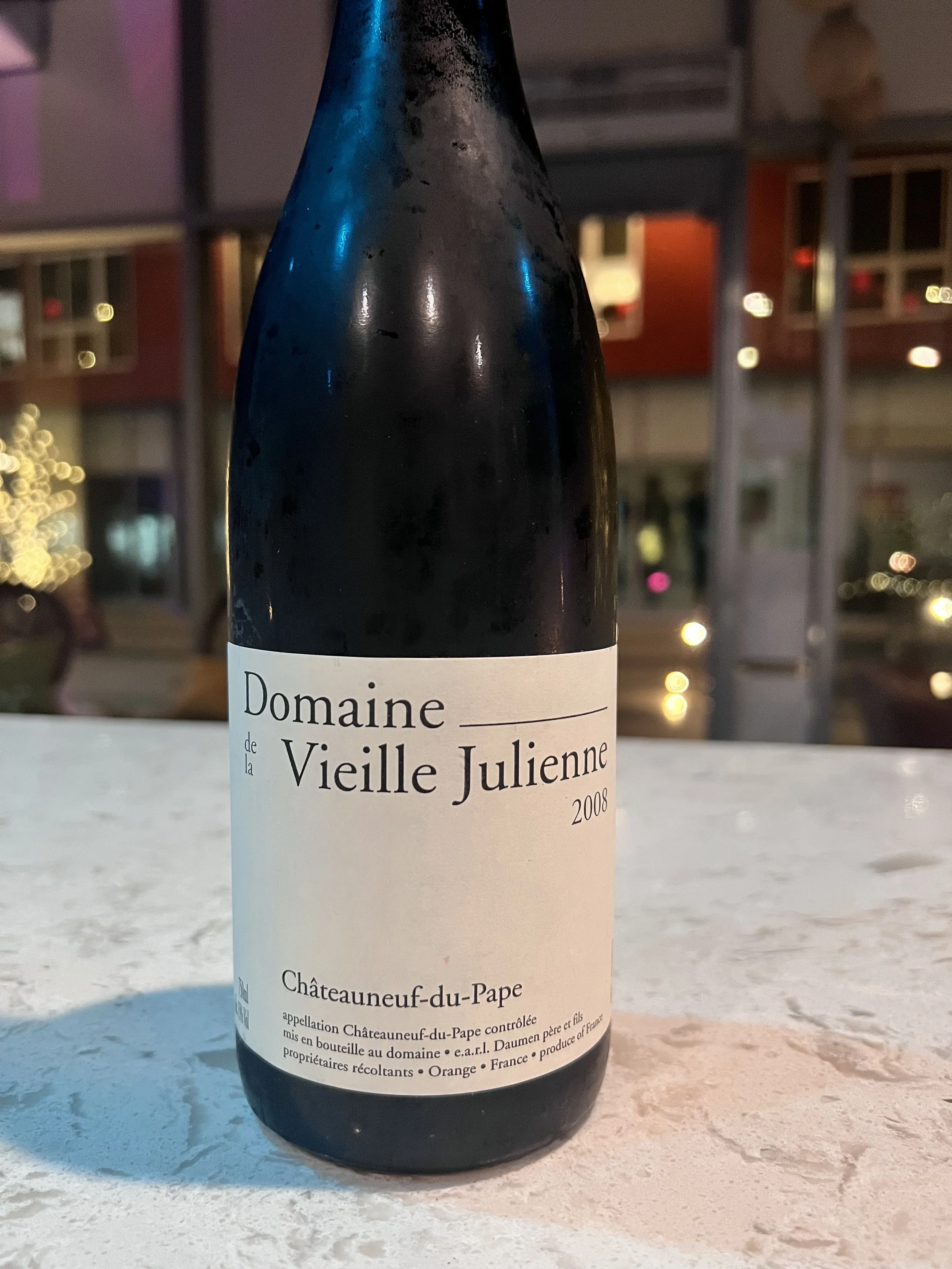 A bottle of Châteauneuf du Pape wine from 2008 on a white table at night with blurred lights in the background.