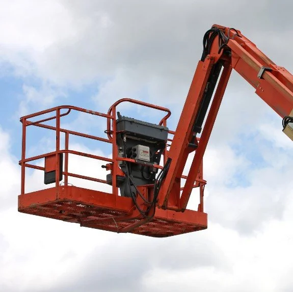 Aerial work platform or cherry picker with an orange arm and platform against a cloudy sky background.
