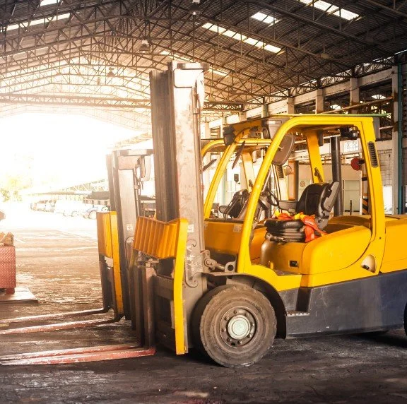 Yellow forklift inside a warehouse with sunlight pouring in from large open doors.