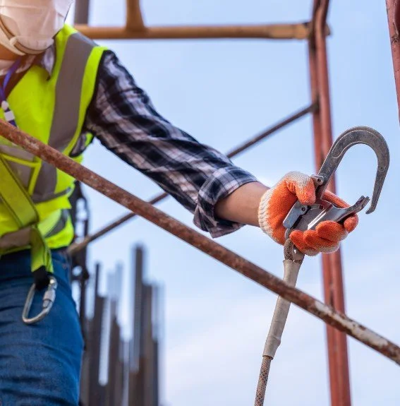 A construction worker holding a steel hook and safety rope on a building site.
