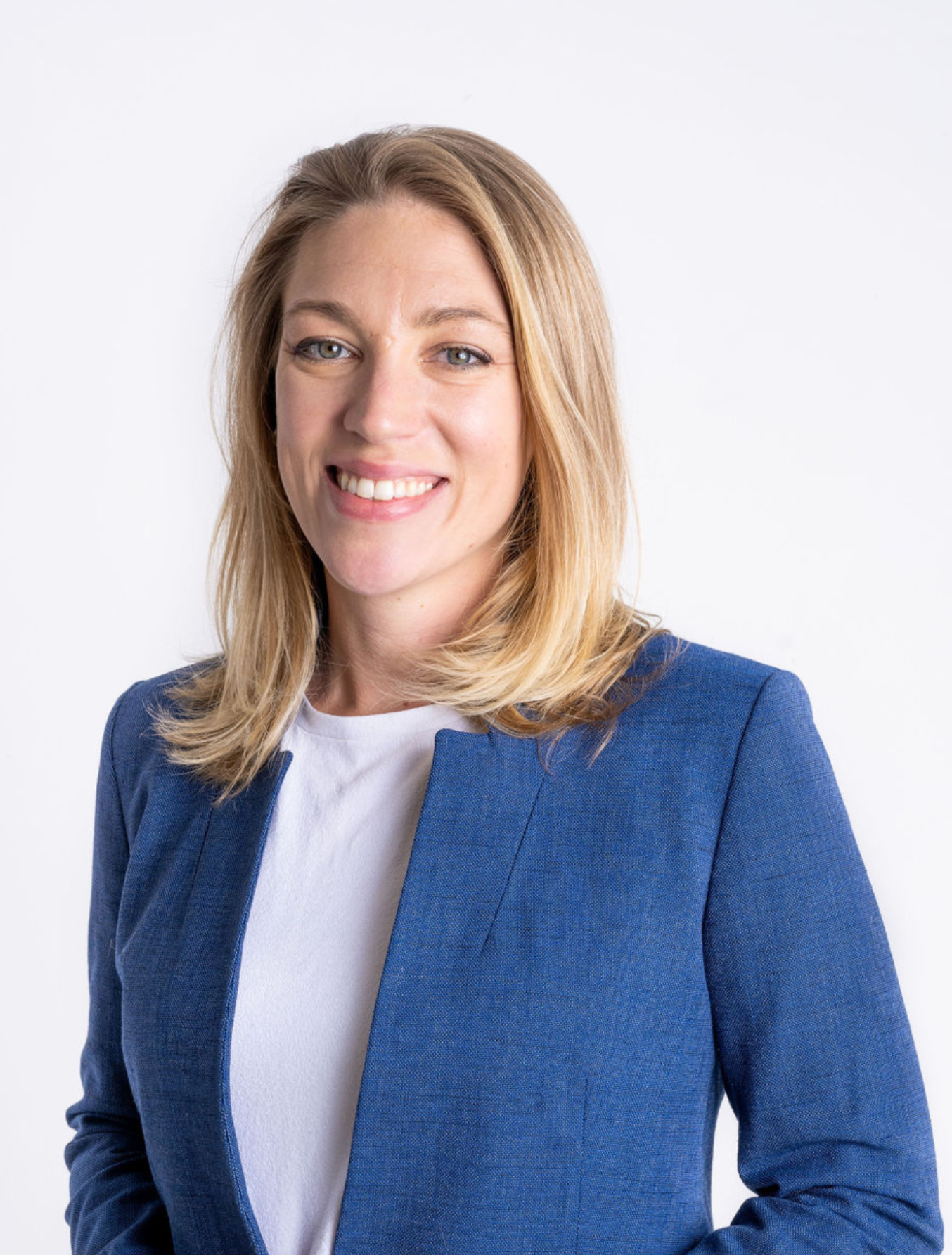 Professional woman with shoulder-length blonde hair, wearing a blue blazer and white shirt, smiling against a plain white background.